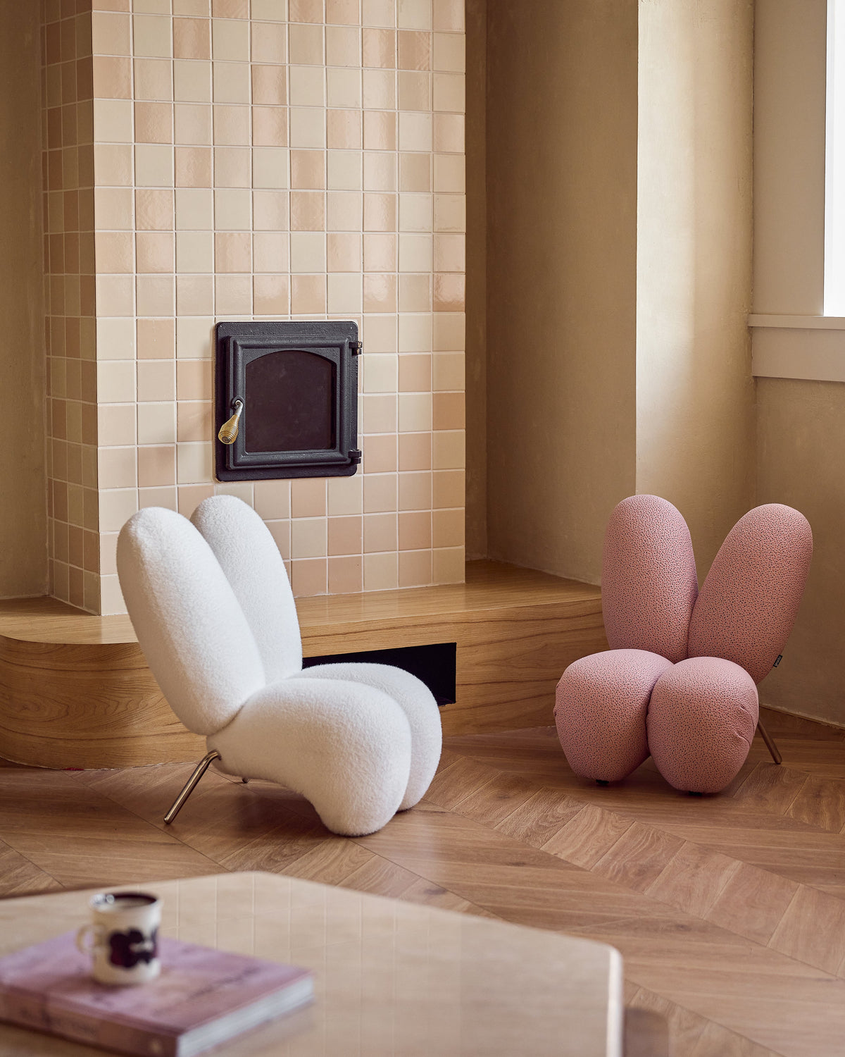 Modern living room with a white chair, pink bunny-shaped chair, and a small table with a cup.