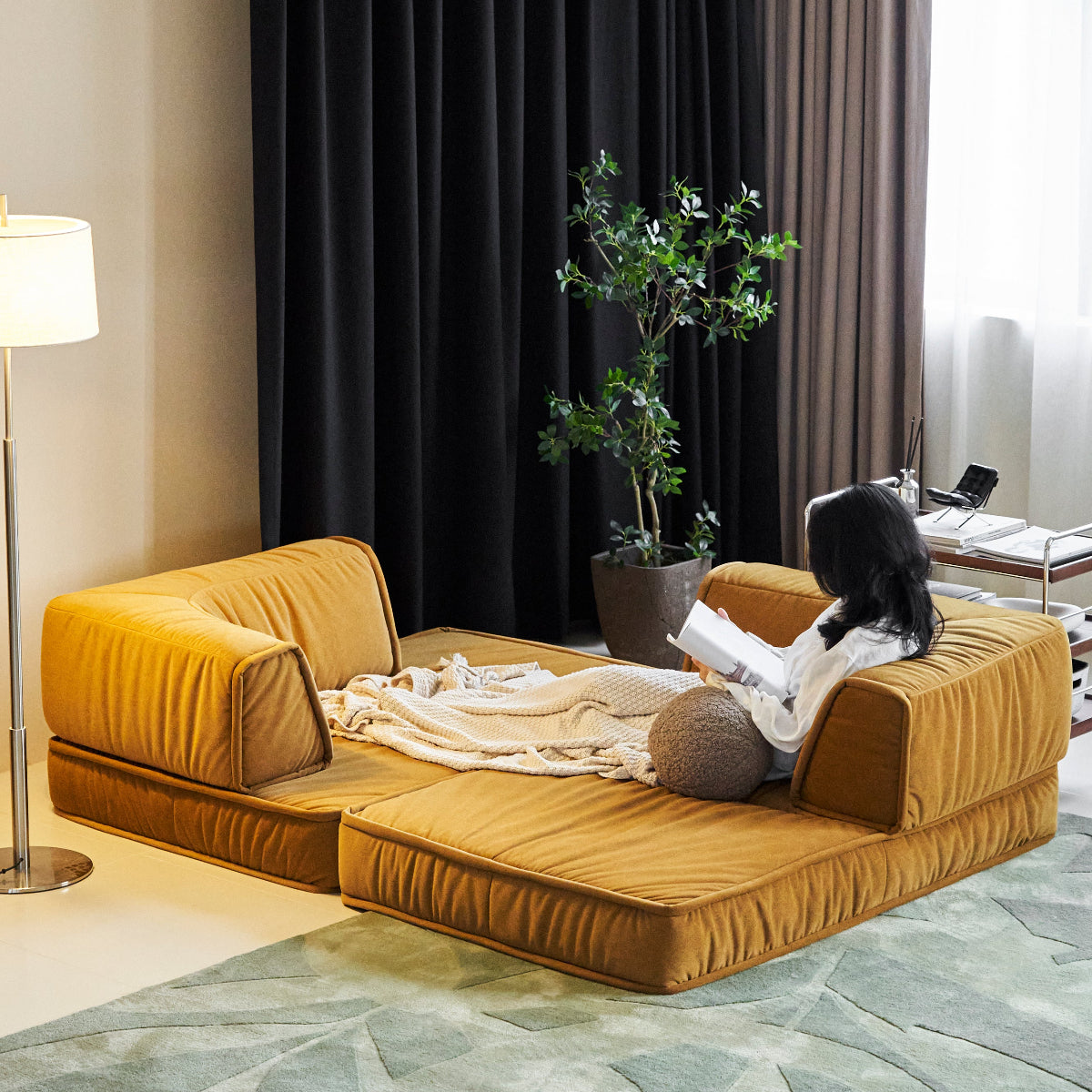 Modern living room with a mustard yellow sofa, black curtains, and a plant.