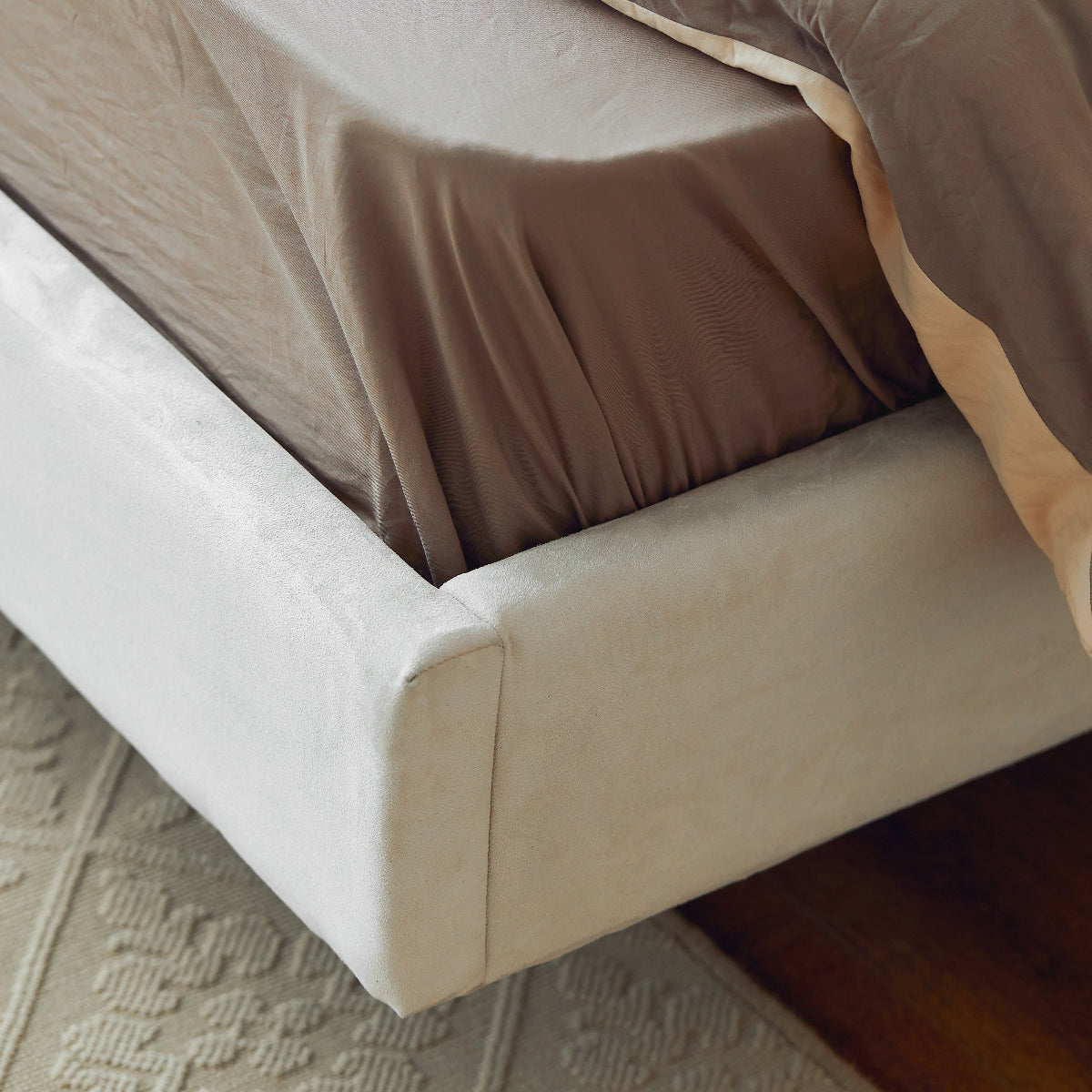 Close-up of a bed with beige bedding on a textured floor.