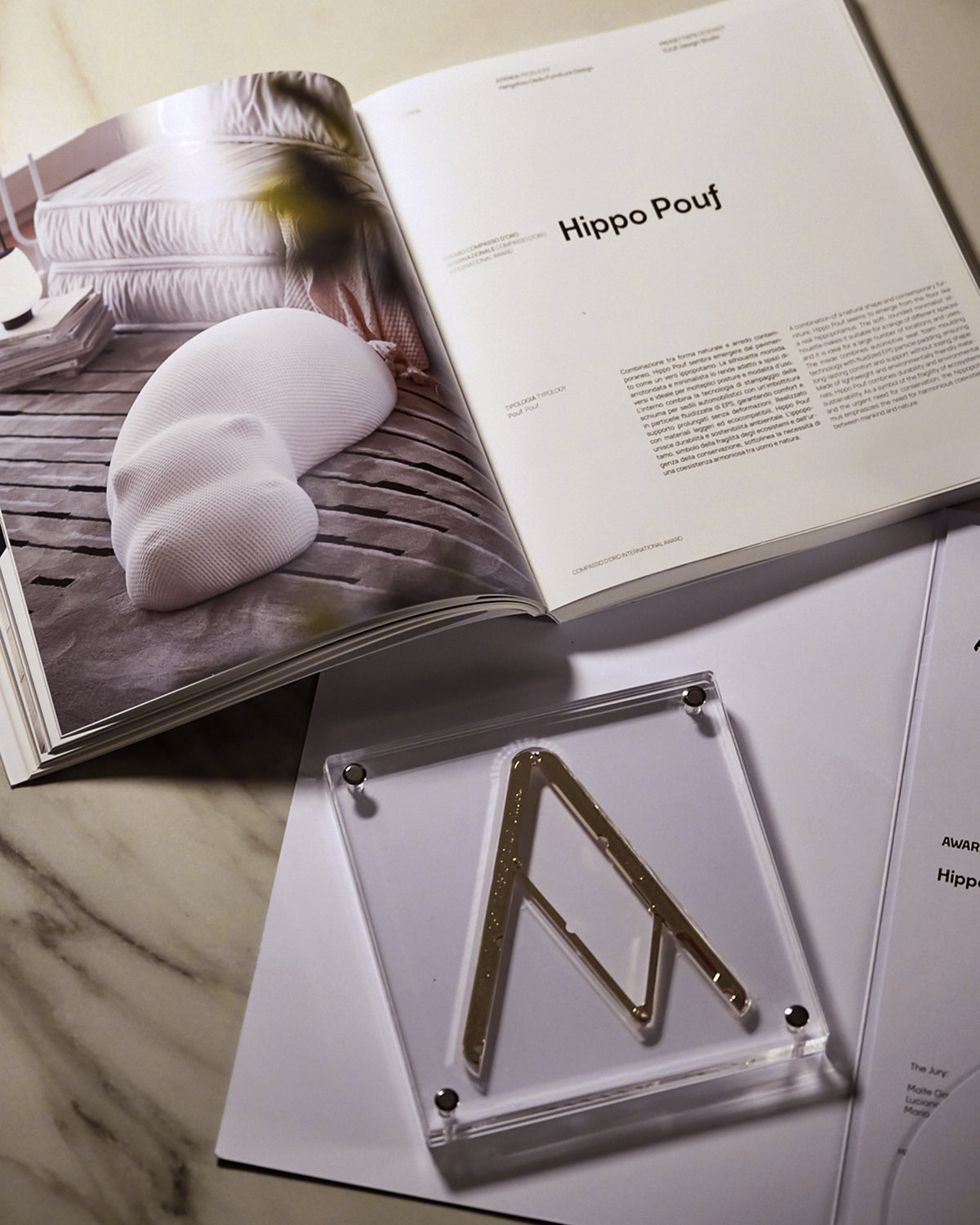 Open book on a marble surface with a clear acrylic stand and 'Hippo Pouf' text.