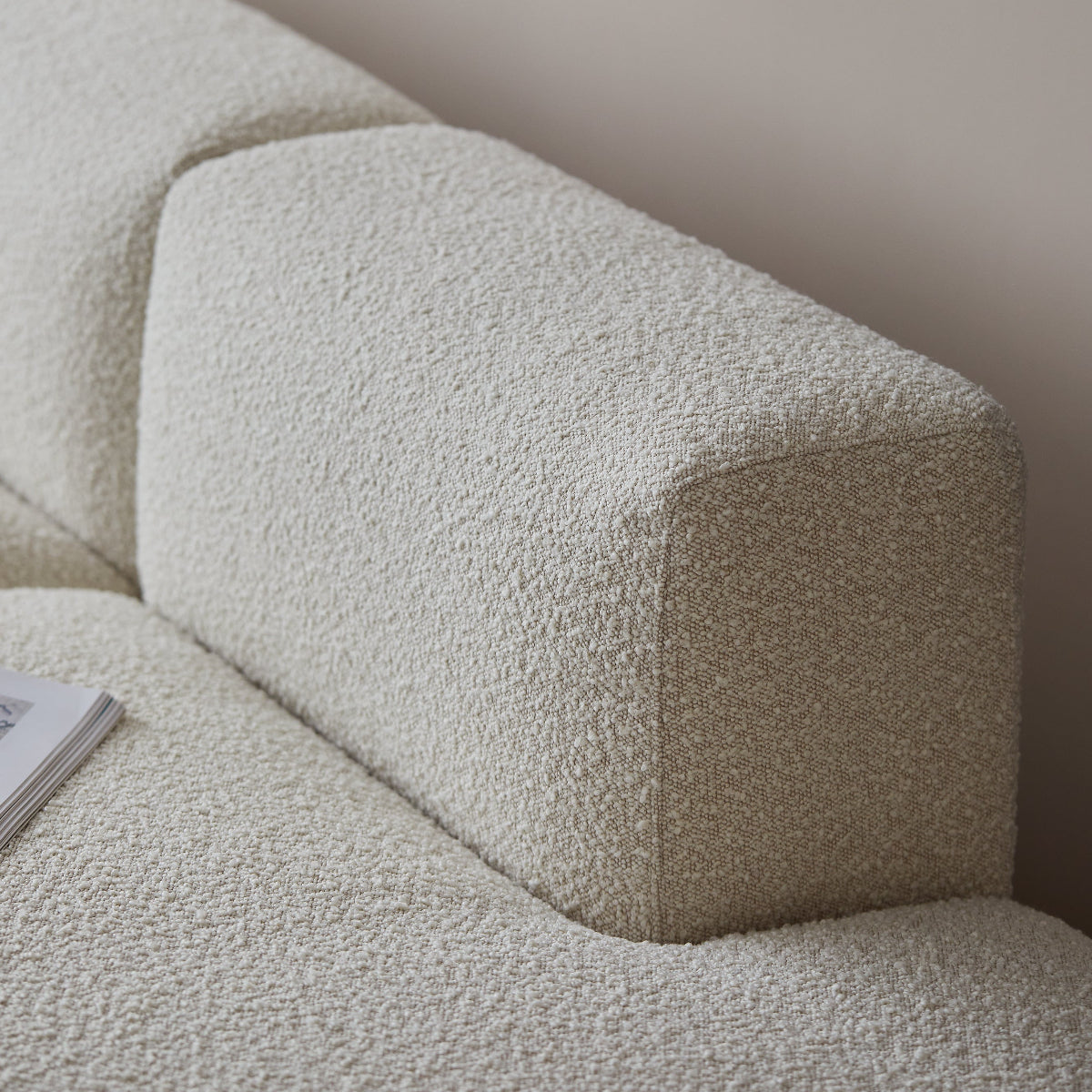 Close-up of a textured boucle sofa cushion in a warm off-white or light beige color, showing the looped fabric detail and part of the sofa arm.