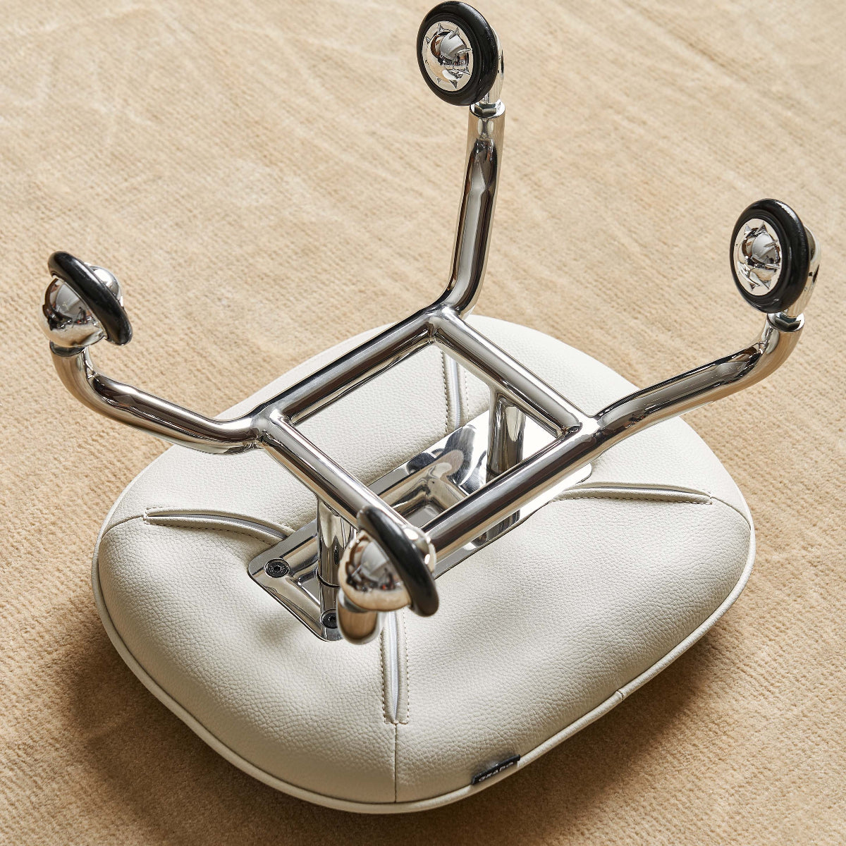 Chrome motorcycle seat bracket on a beige cushion with a wooden background