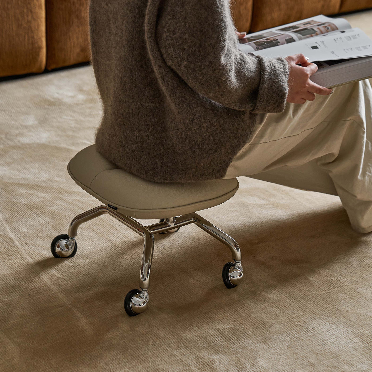 Person sitting on a beige chair reading a newspaper in a living room.