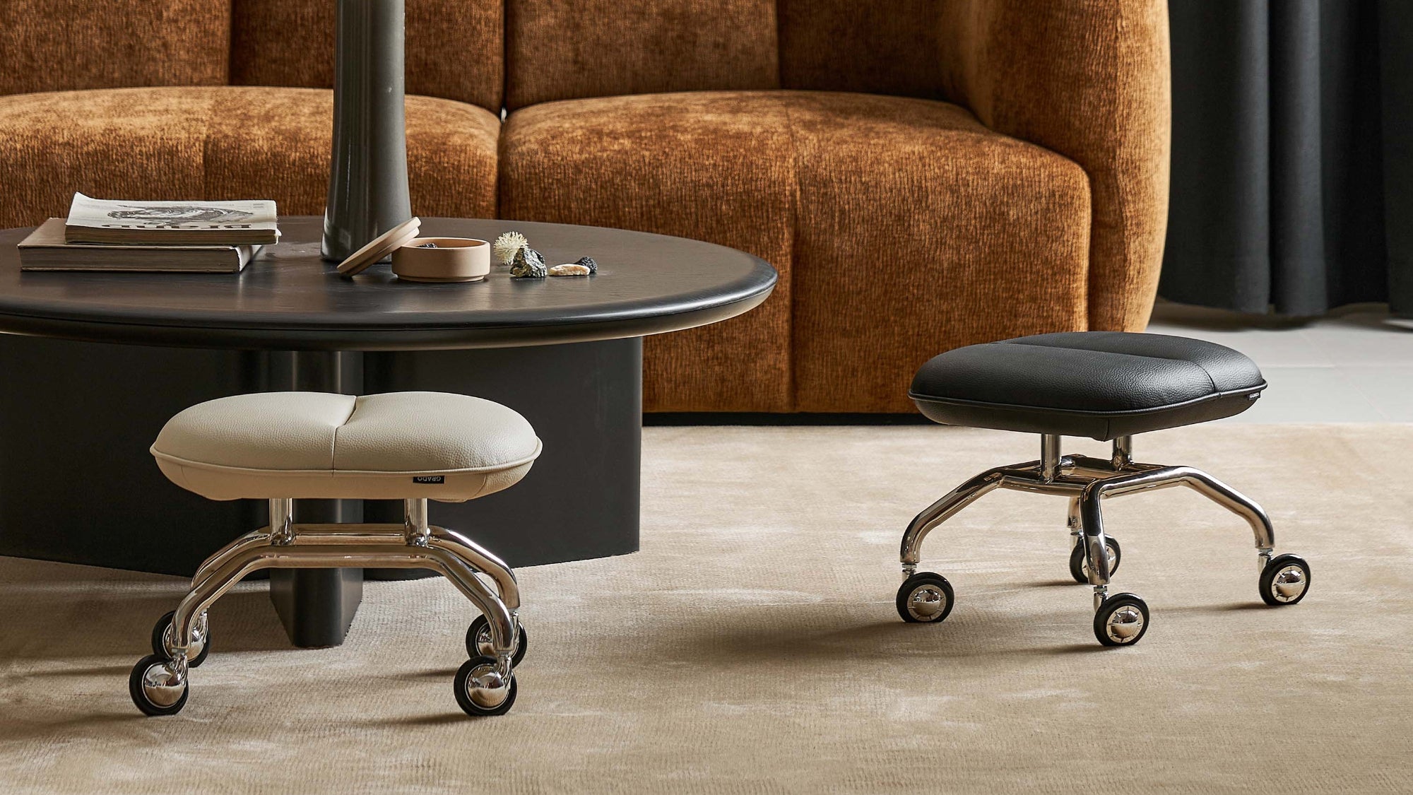 Brown sofa in a living room with a round table and two stools.
