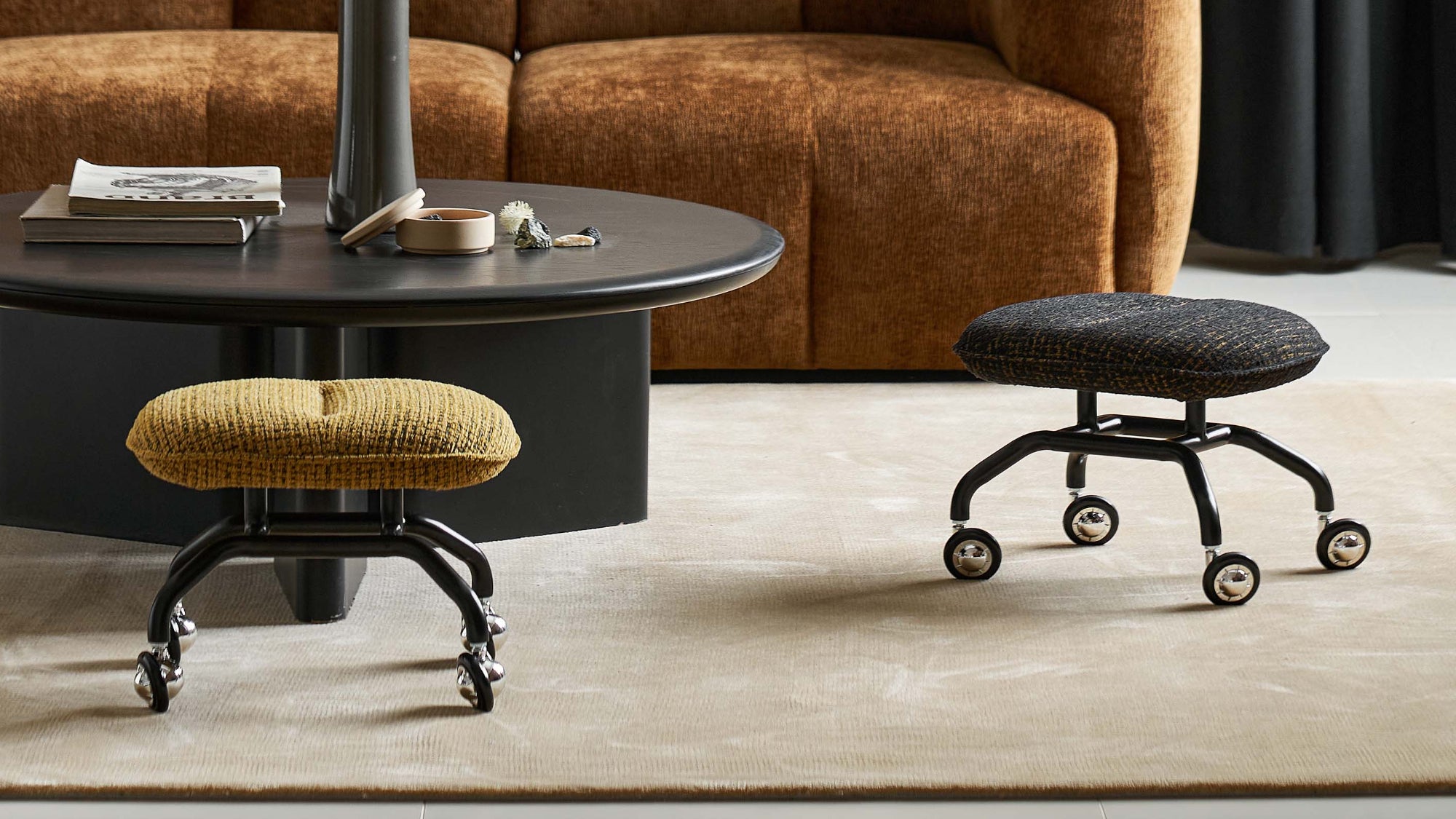 Modern living room with brown sofa, black round table, and stools.