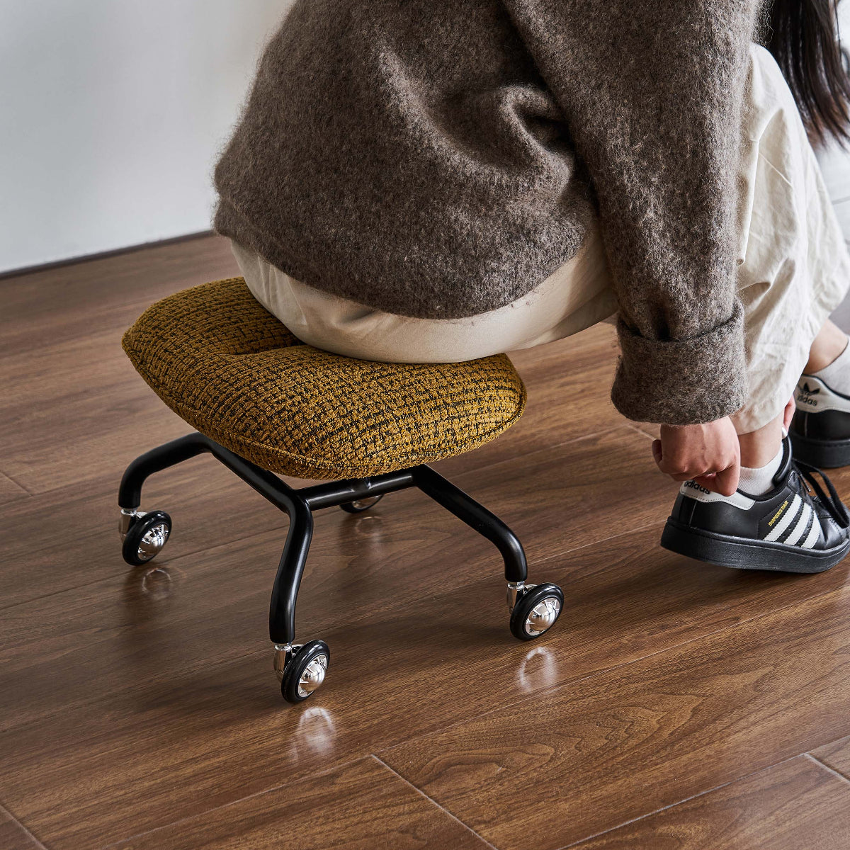 Person using a small office chair on a wooden floor