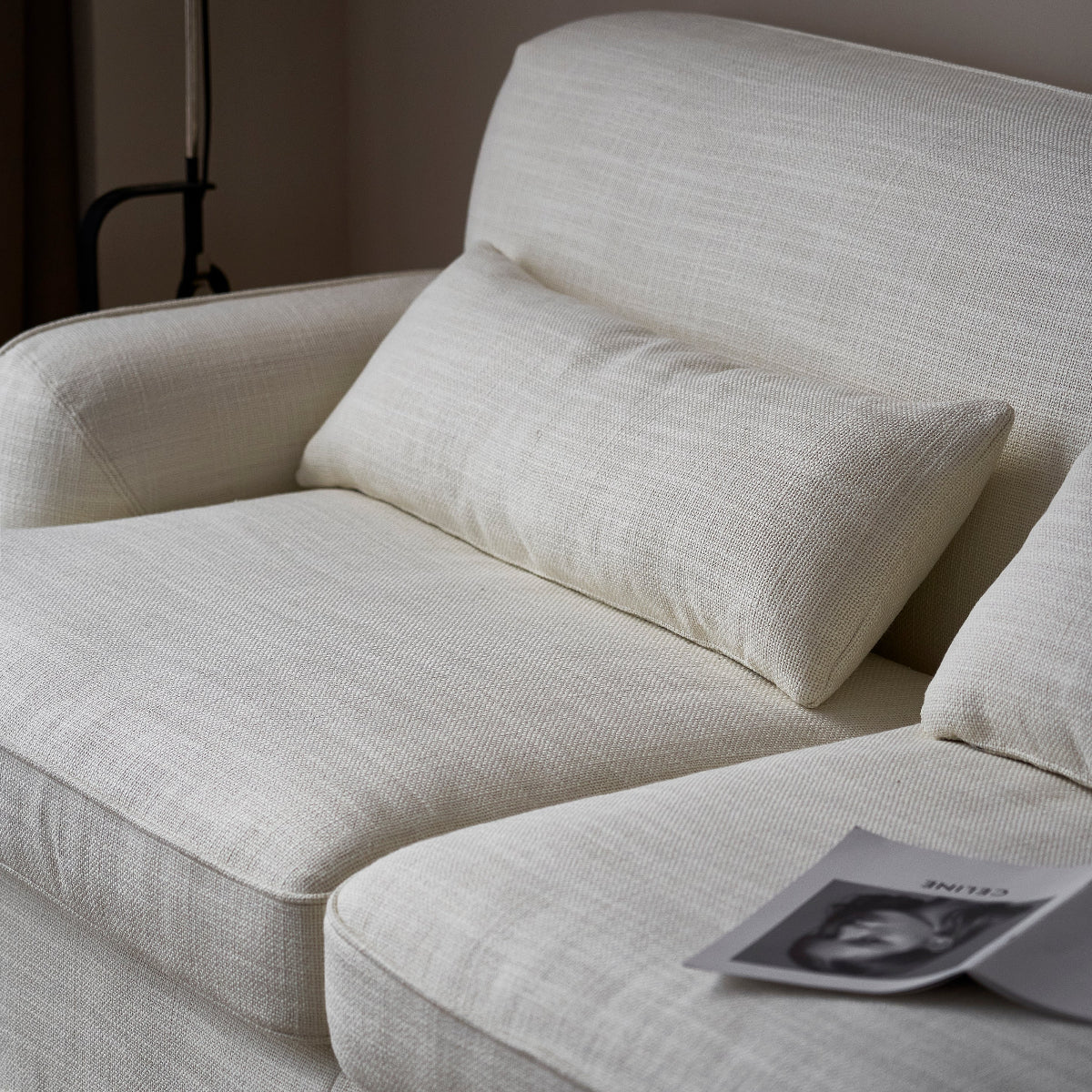 Beige sofa with a pillow and a magazine on a wooden floor.