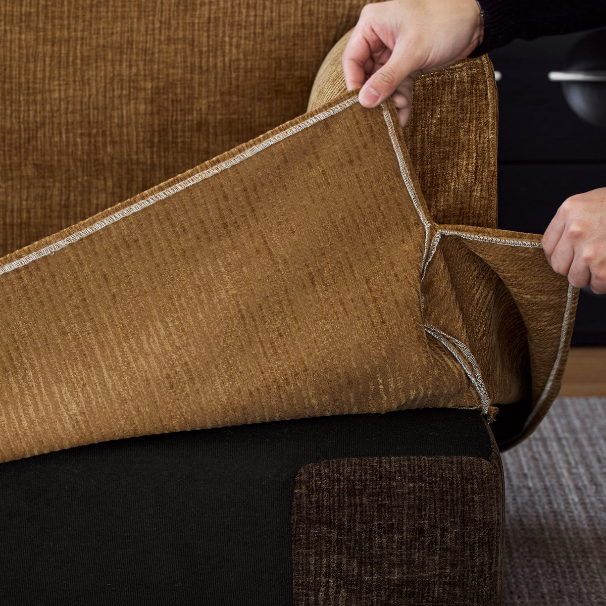 Person adjusting a brown textured sofa cover on a chair.