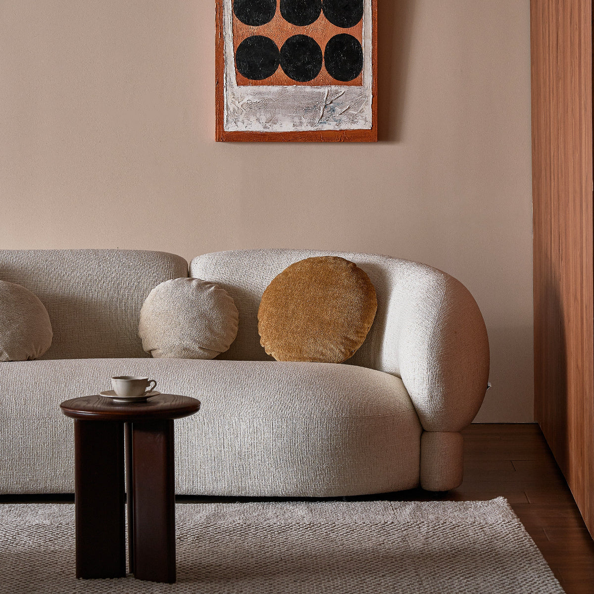 Modern living room with a beige sofa, round wooden table, and abstract wall art.