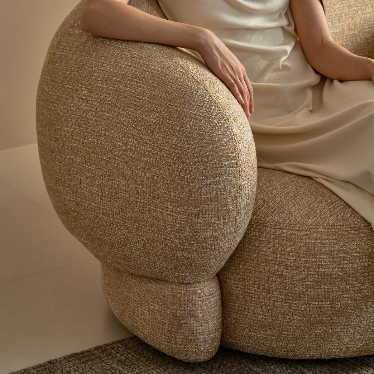 Woman in a beige dress sitting on a textured beige chair.
