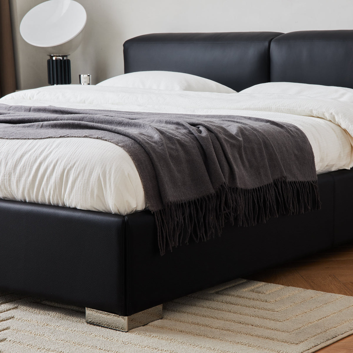 Black leather bed with white bedding and a gray throw blanket in a bedroom setting.
