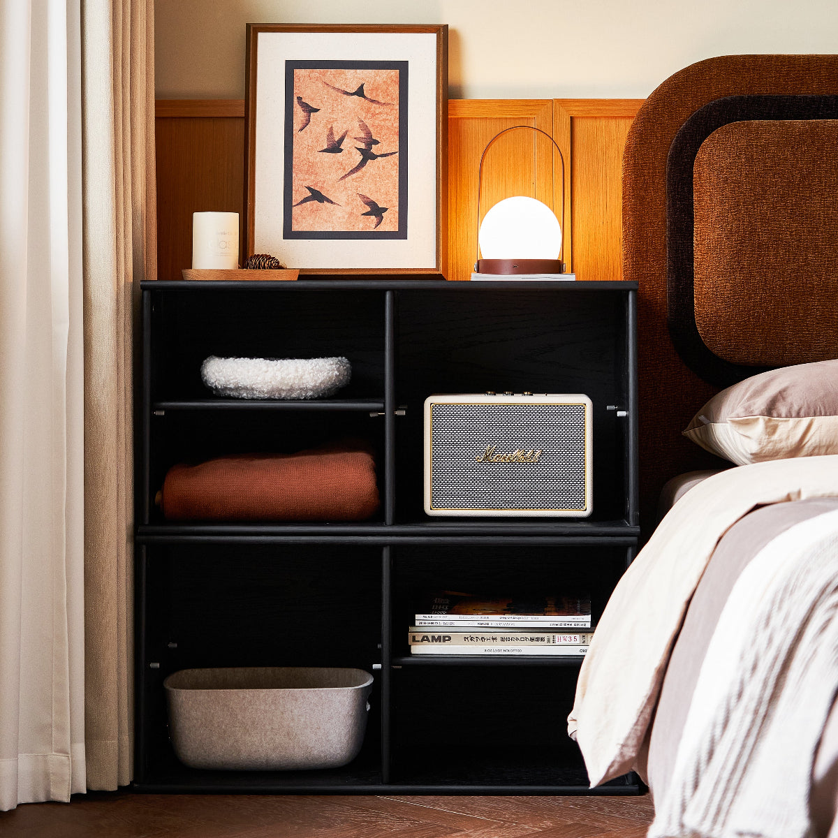 Black cube shelf in a bedroom with books, a basket, and a lamp.