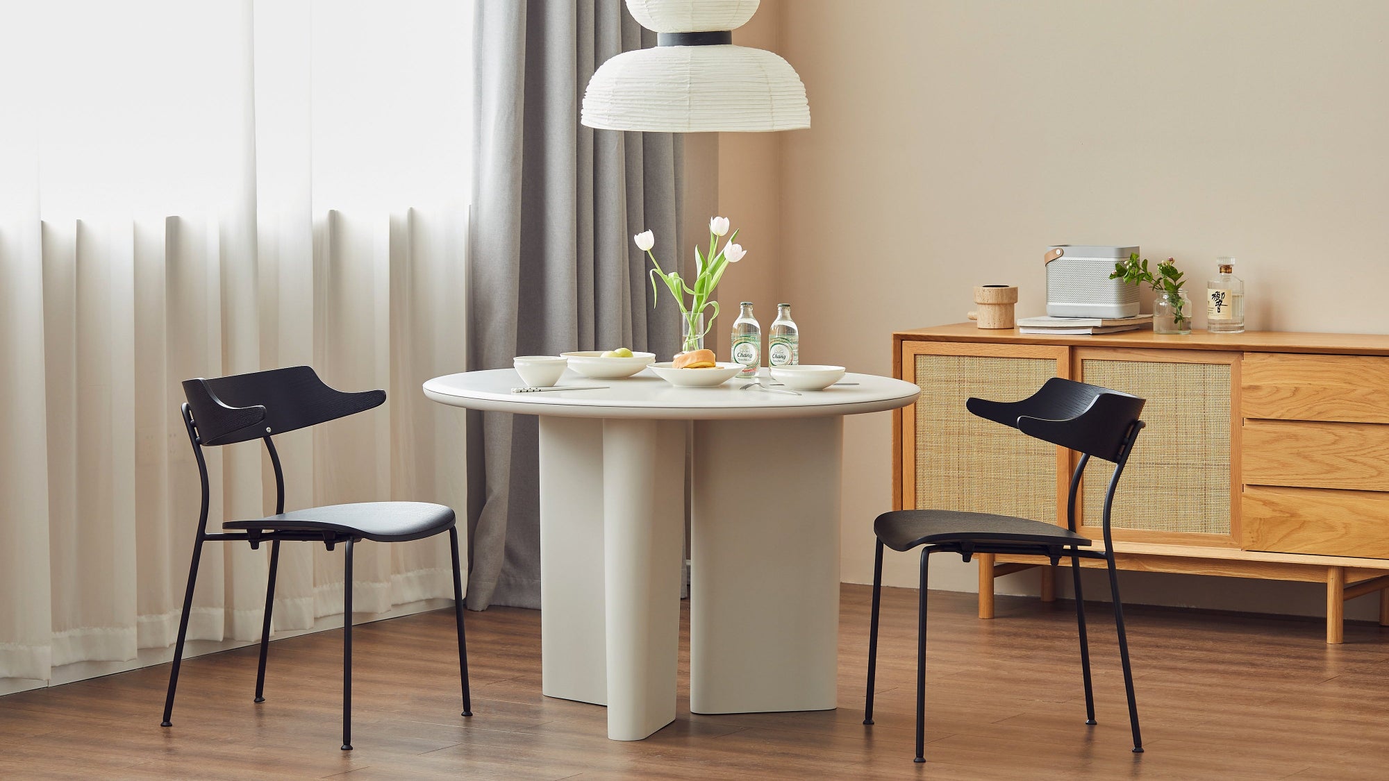 Modern dining area with a round table and two black chairs in a well-lit room.