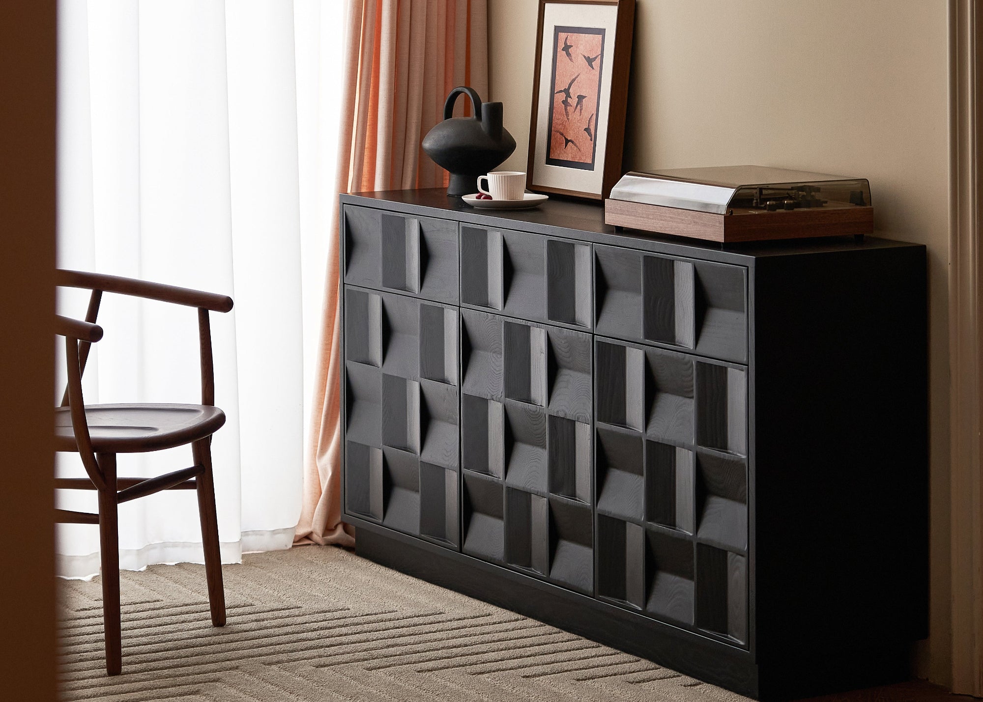 Black textured sideboard with decorative items in a room with curtains and a chair.