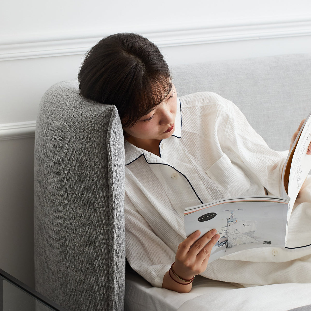 Woman reading a magazine in bed with a gray headboard