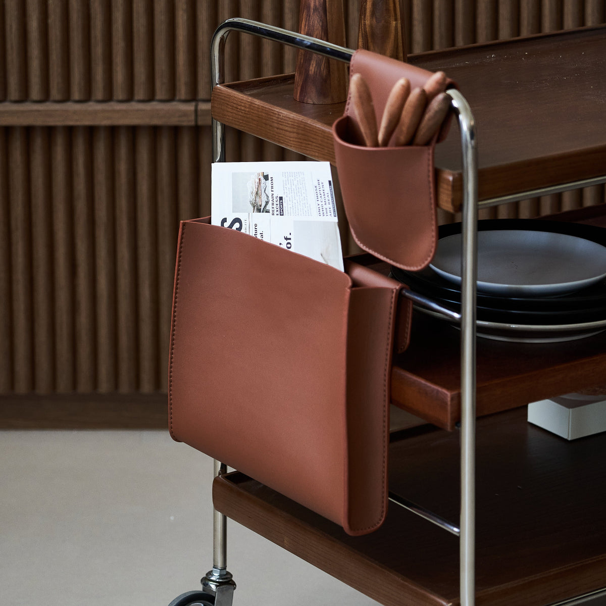 Wooden trolley with brown leather bags and plates on a wooden floor.