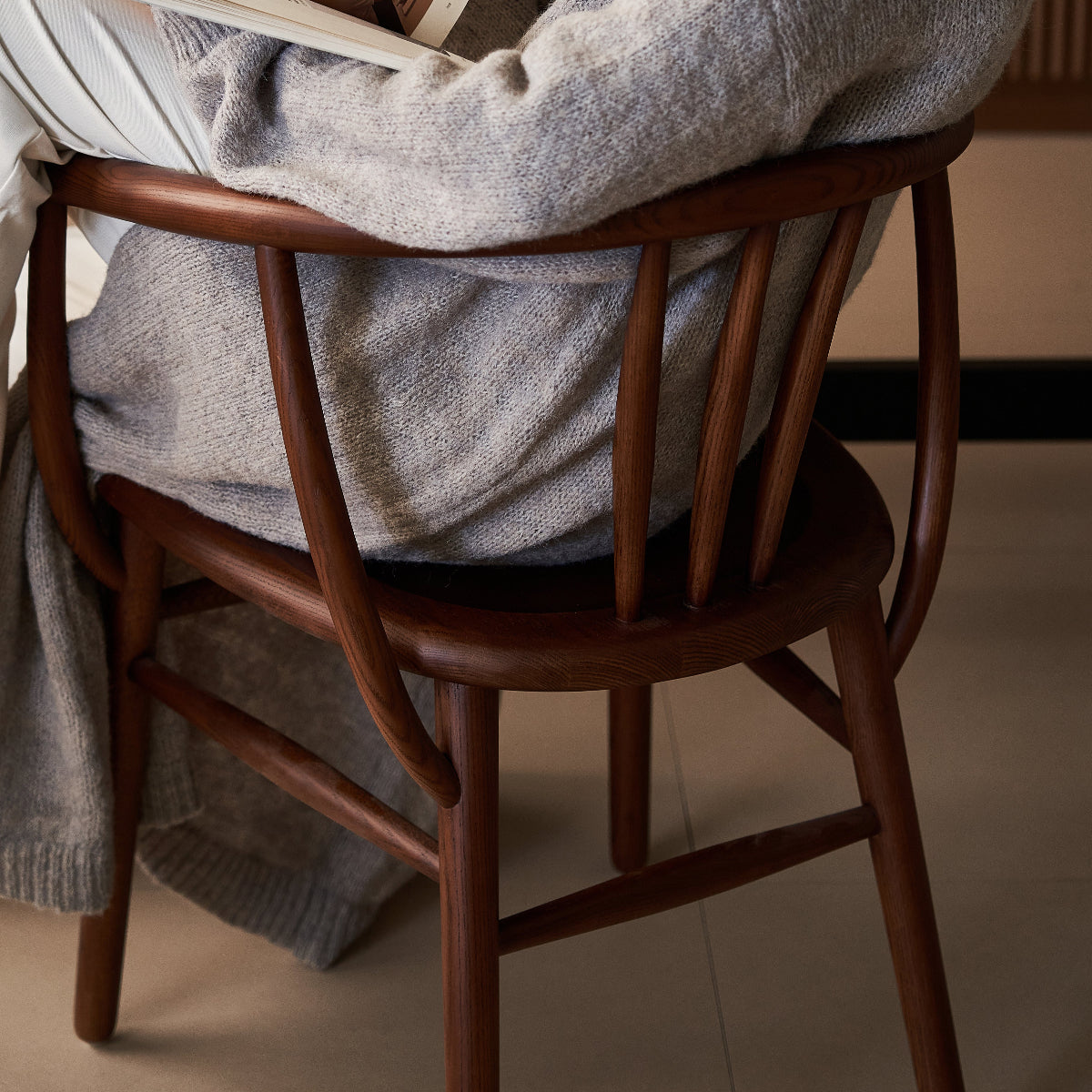 Person sitting in a chair reading a book with a warm, cozy atmosphere.