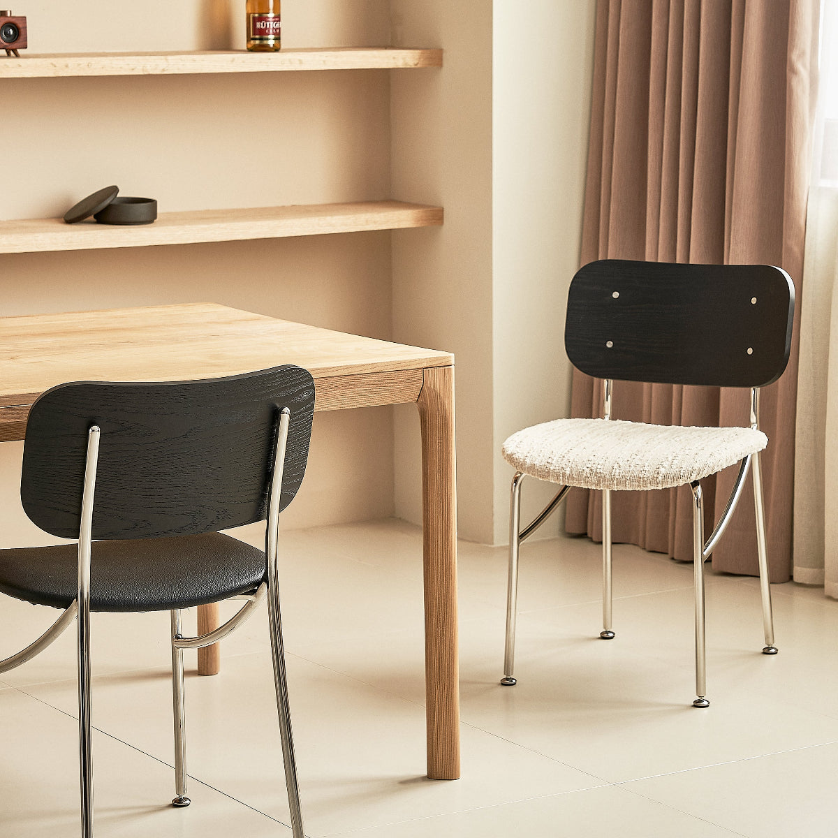 Two black chairs at a wooden table with shelves and curtains in the background.