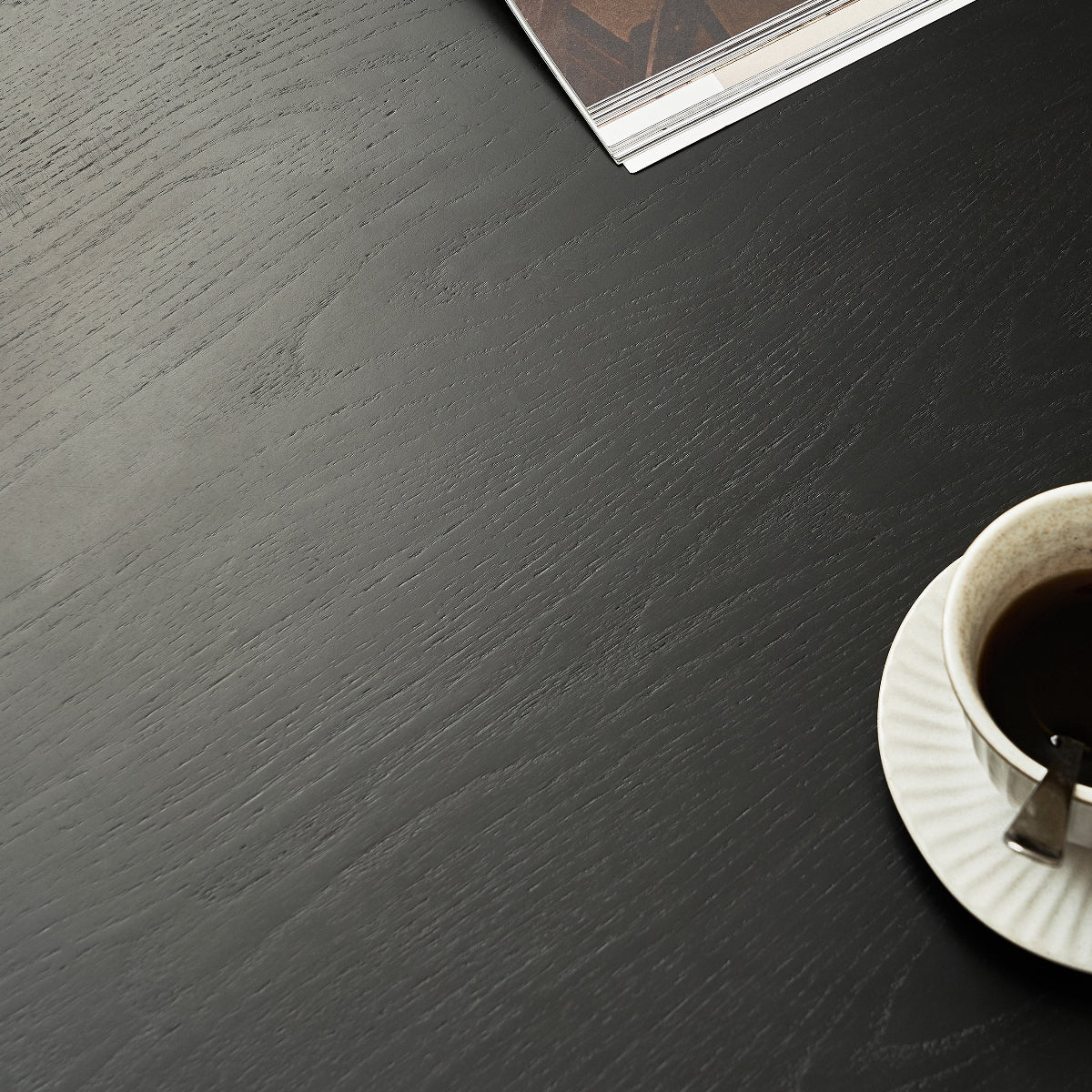 Open book with a patterned cover on a dark wooden surface next to a cup of coffee.
