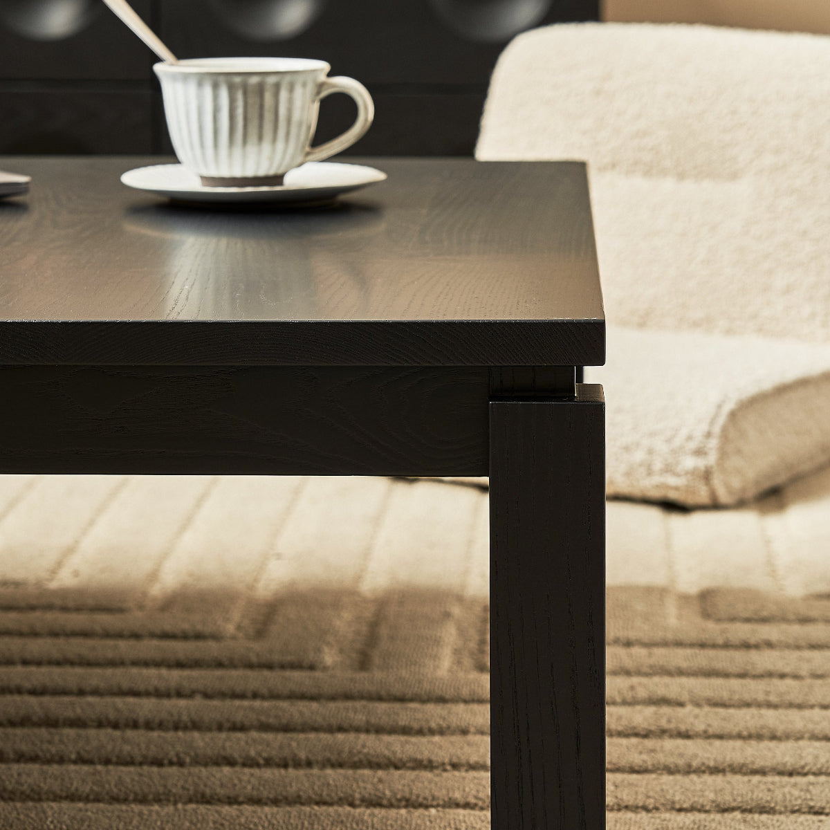 Black coffee table with a white teacup and saucer on a beige carpeted floor.