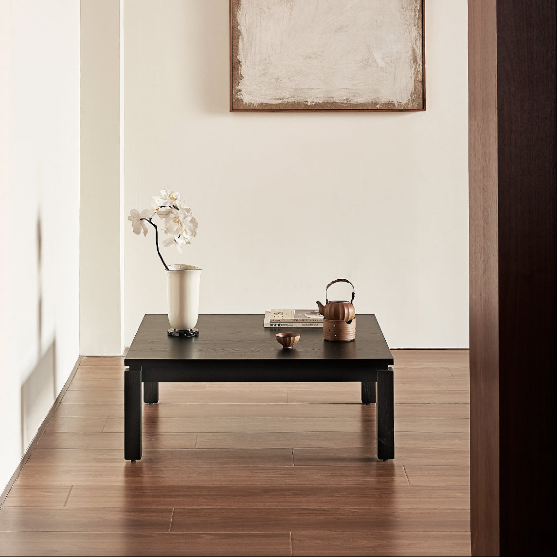 Modern living room with a black coffee table, vase with flowers, and abstract painting on the wall.