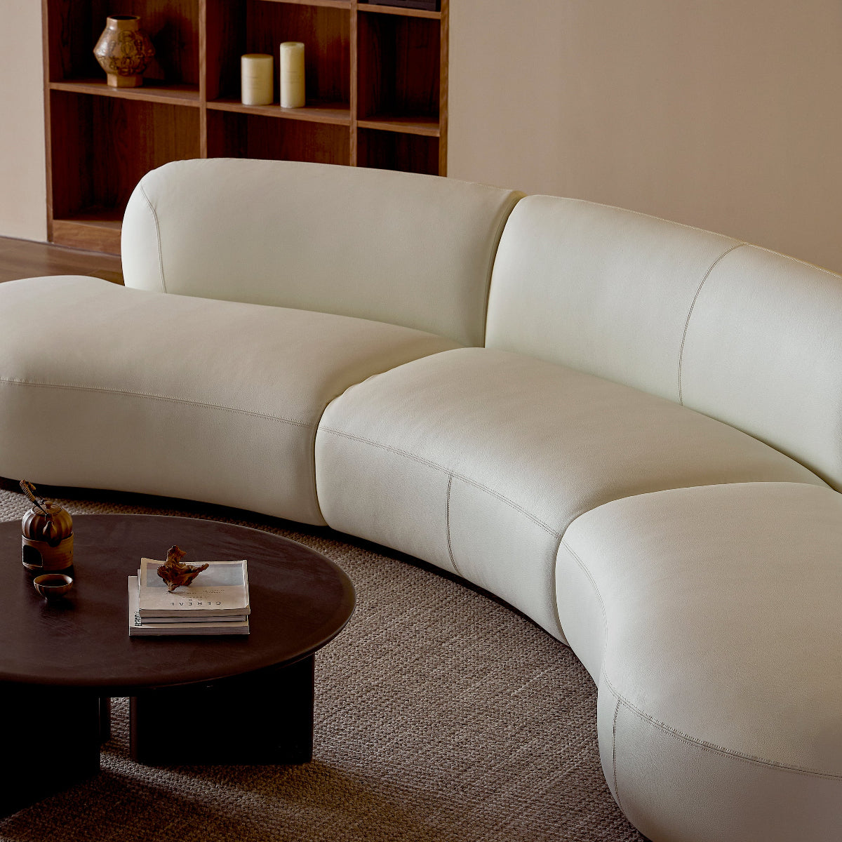 White curved sofa in a living room with a bookshelf and coffee table.