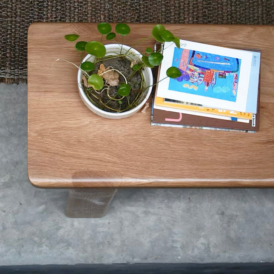 Wooden table with a small potted plant and colorful book on a concrete floor.