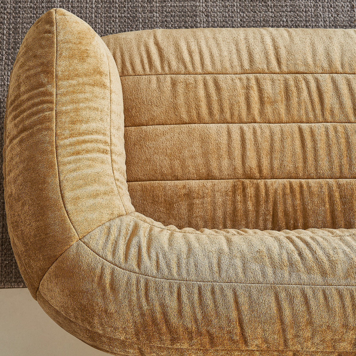 Close-up of a textured beige sofa against a textured brown wall.