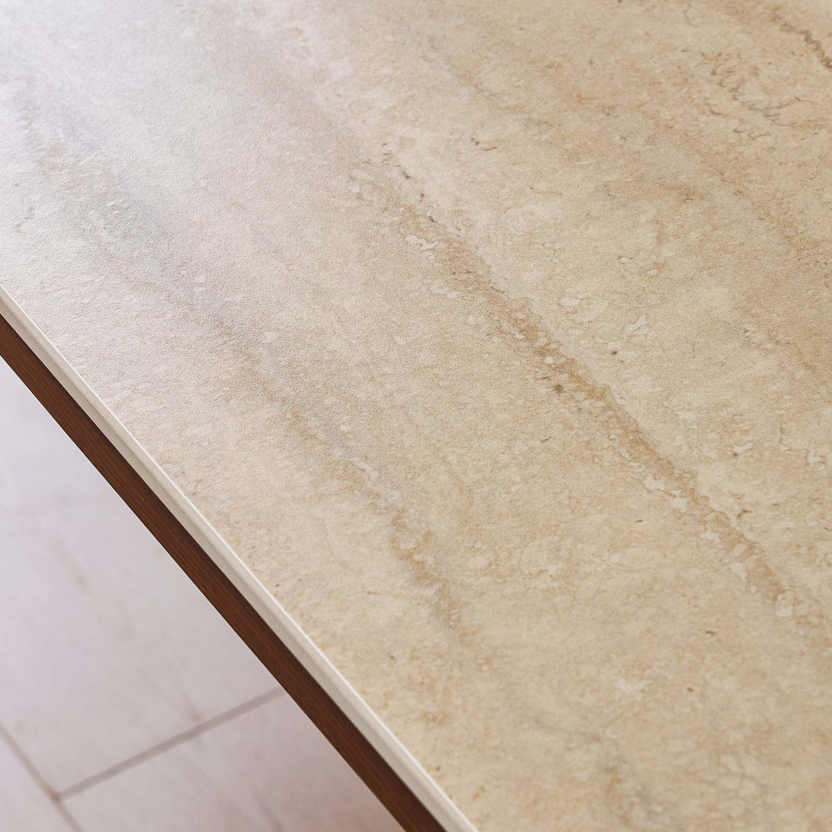 Close-up of a light beige stone or tile surface with natural marbled veining, shown at an angle over a light wood floor.