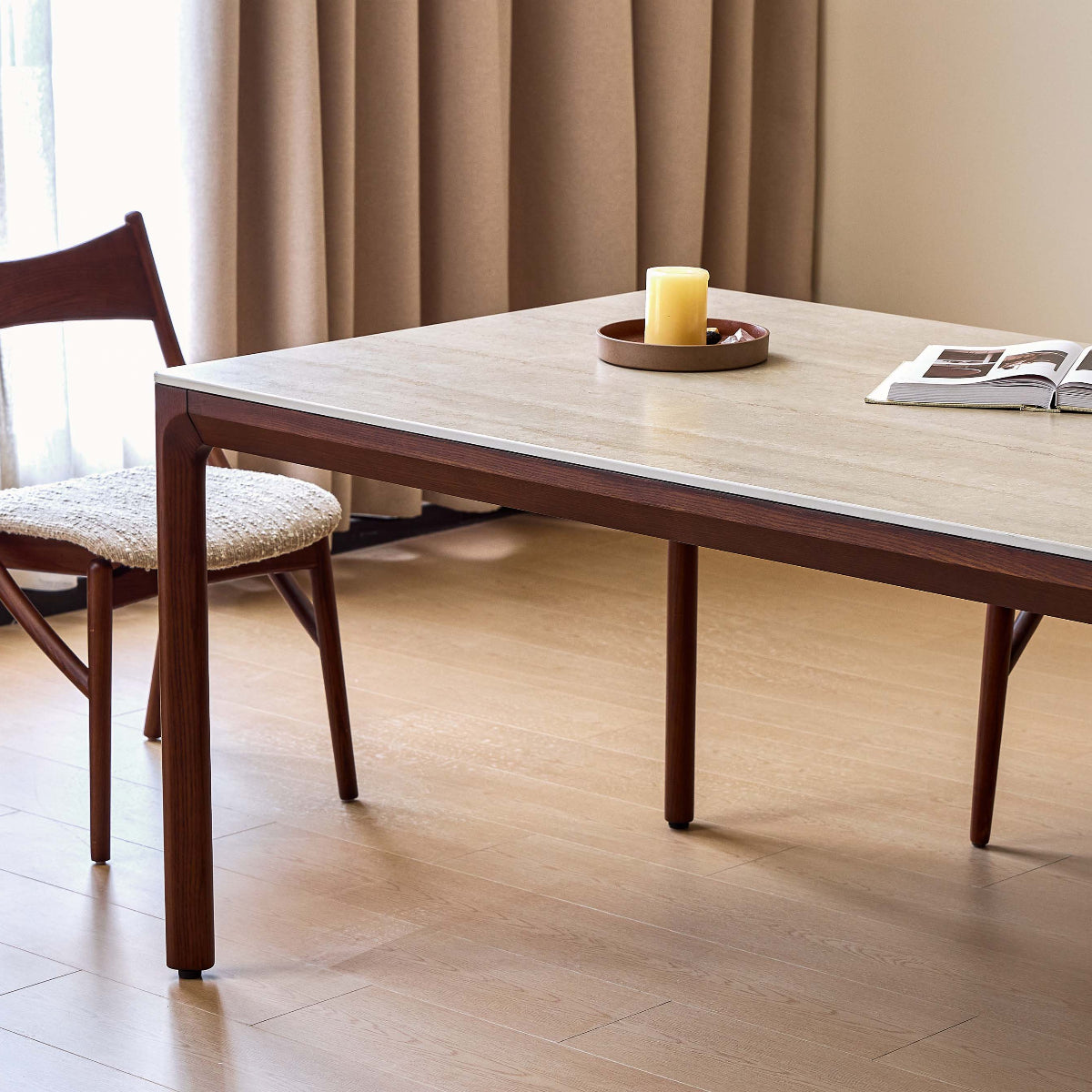 A rectangular dining table with a light wood top and dark brown wooden legs, accompanied by two matching wooden chairs in a bright, modern dining room setting.