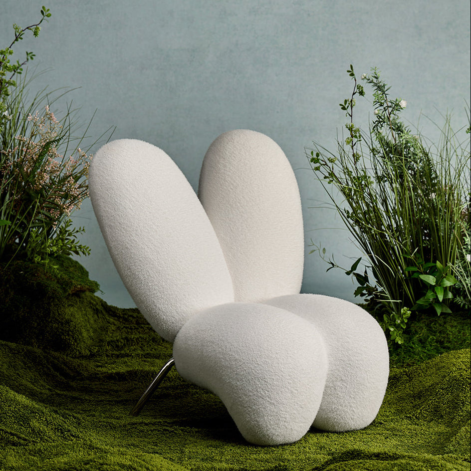 Modern white chair in a natural setting with plants and a textured wall.