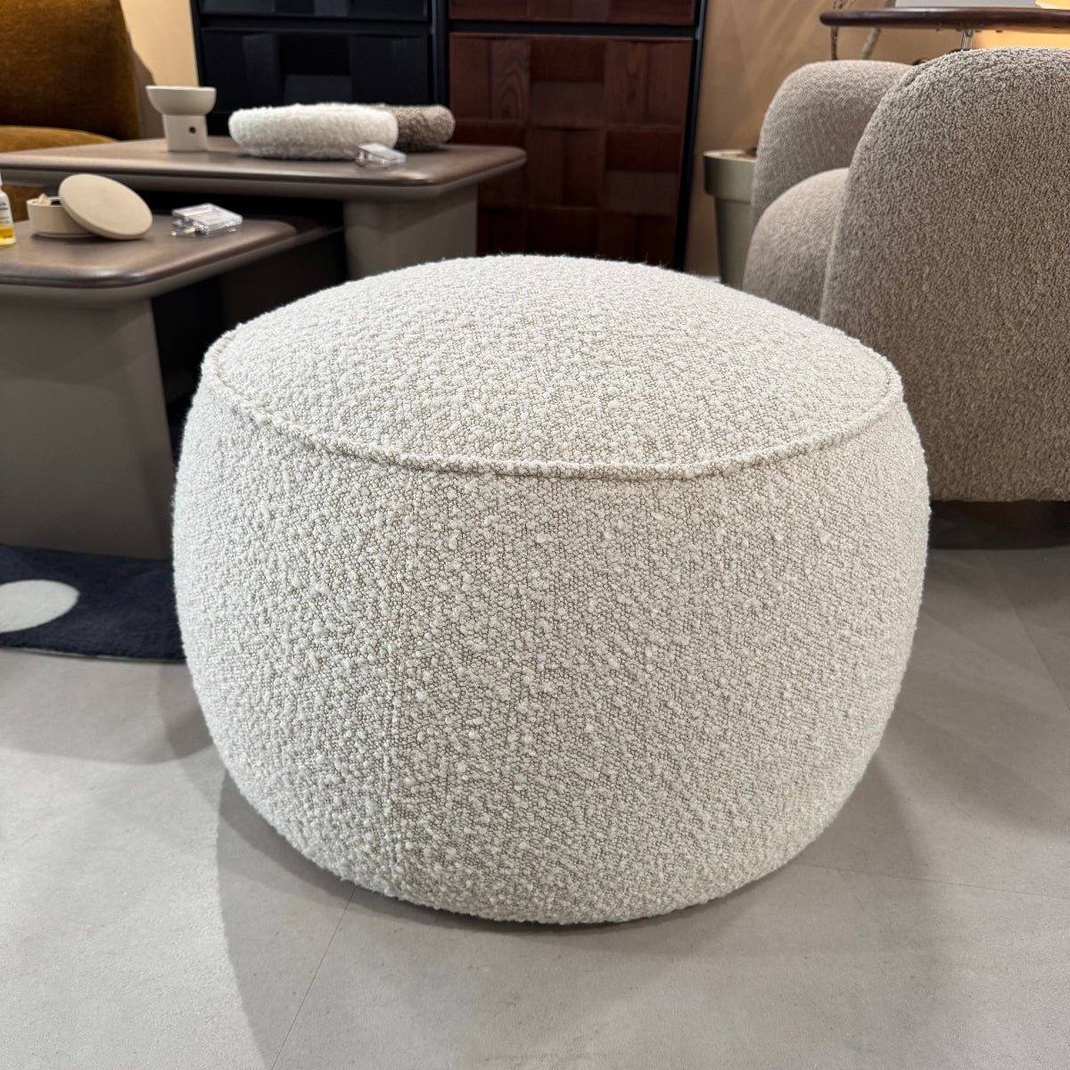 Close-up of a textured gray ottoman in a room with furniture and decor.