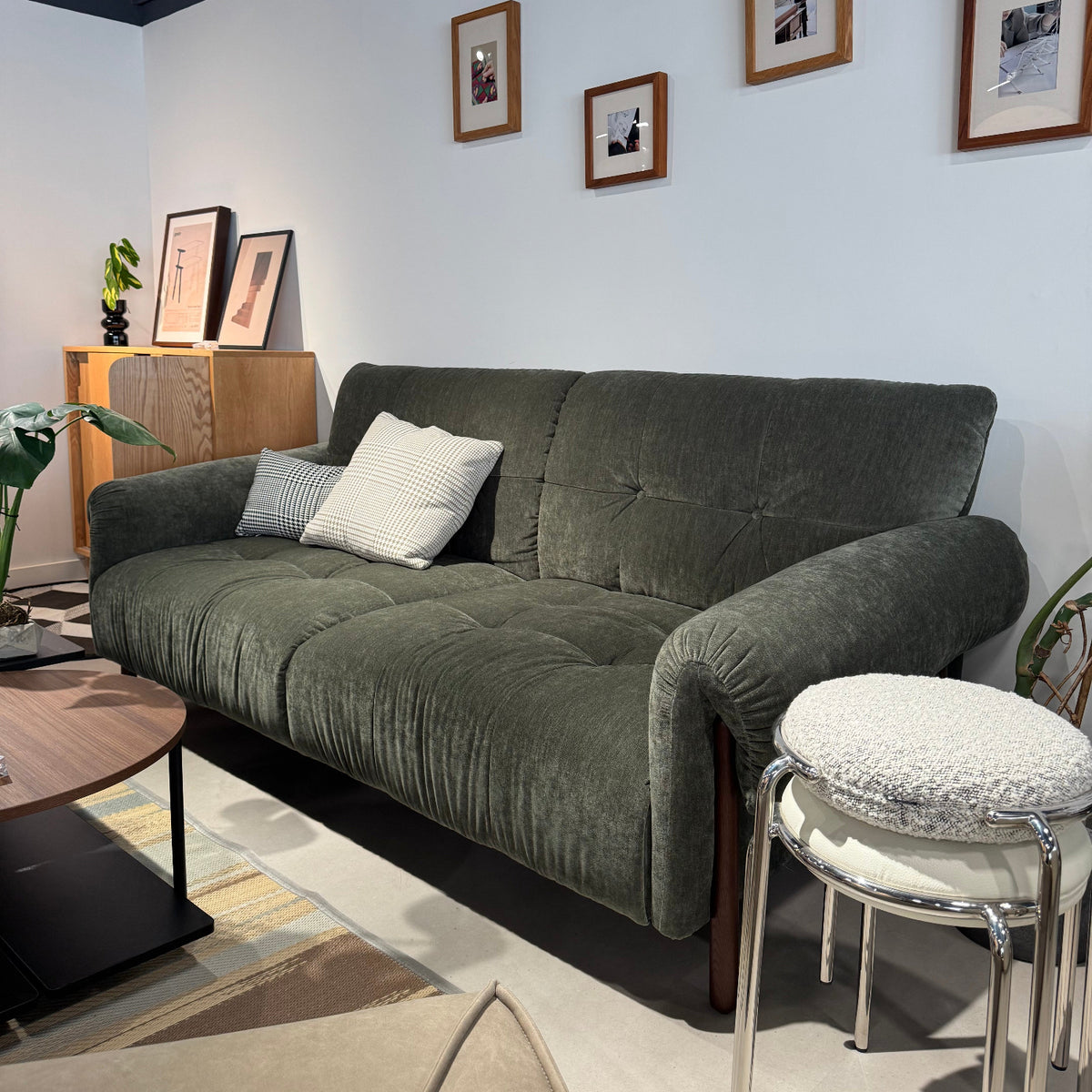 Green sofa with cushions in a room with framed pictures on the wall.
