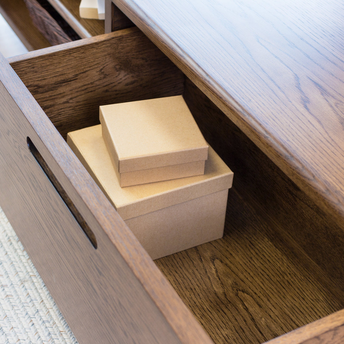 Wooden drawer with two beige boxes inside on a wooden surface.