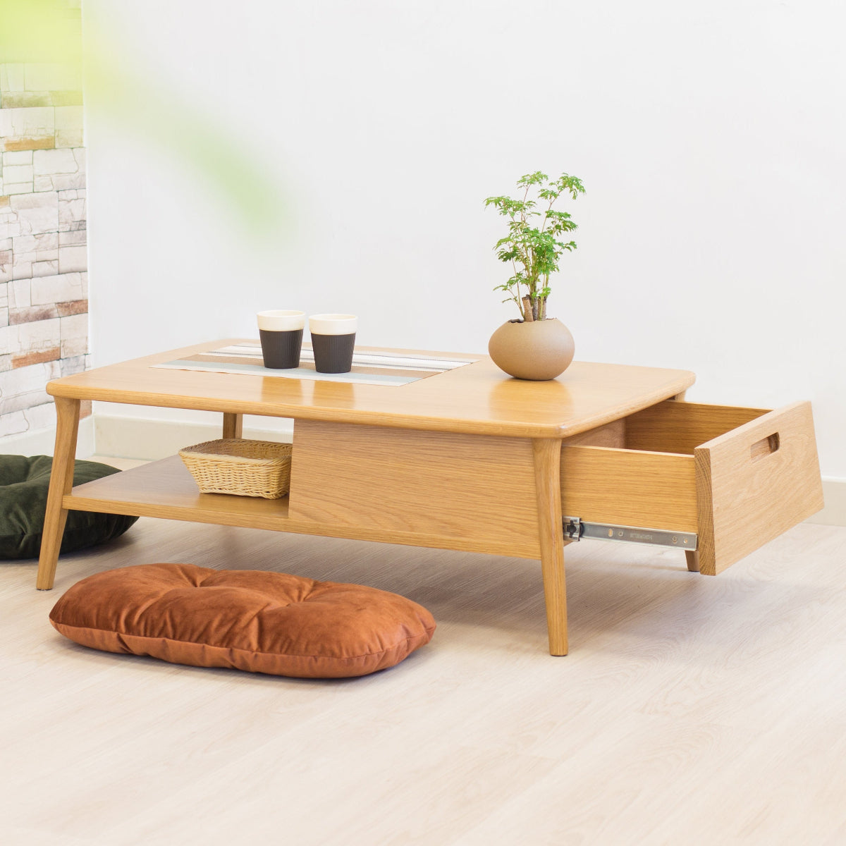 Wooden coffee table with a drawer, plant, and cushions in a minimalistic room.