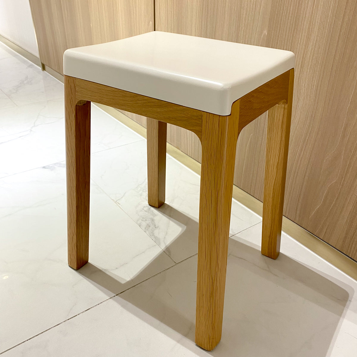 Wooden stool with a white cushion on a tiled floor.