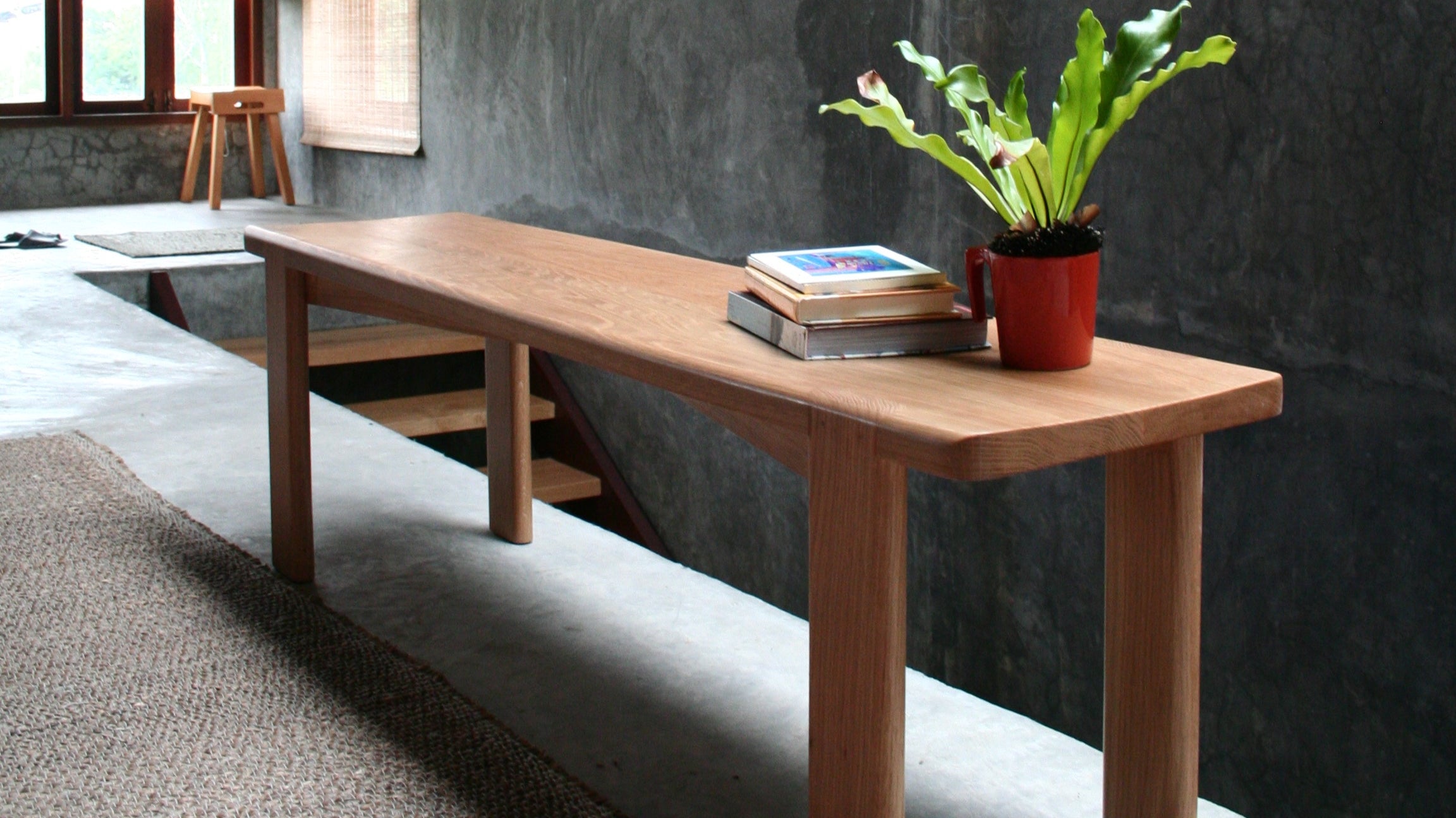 Wooden bench with a plant and books against a textured wall.