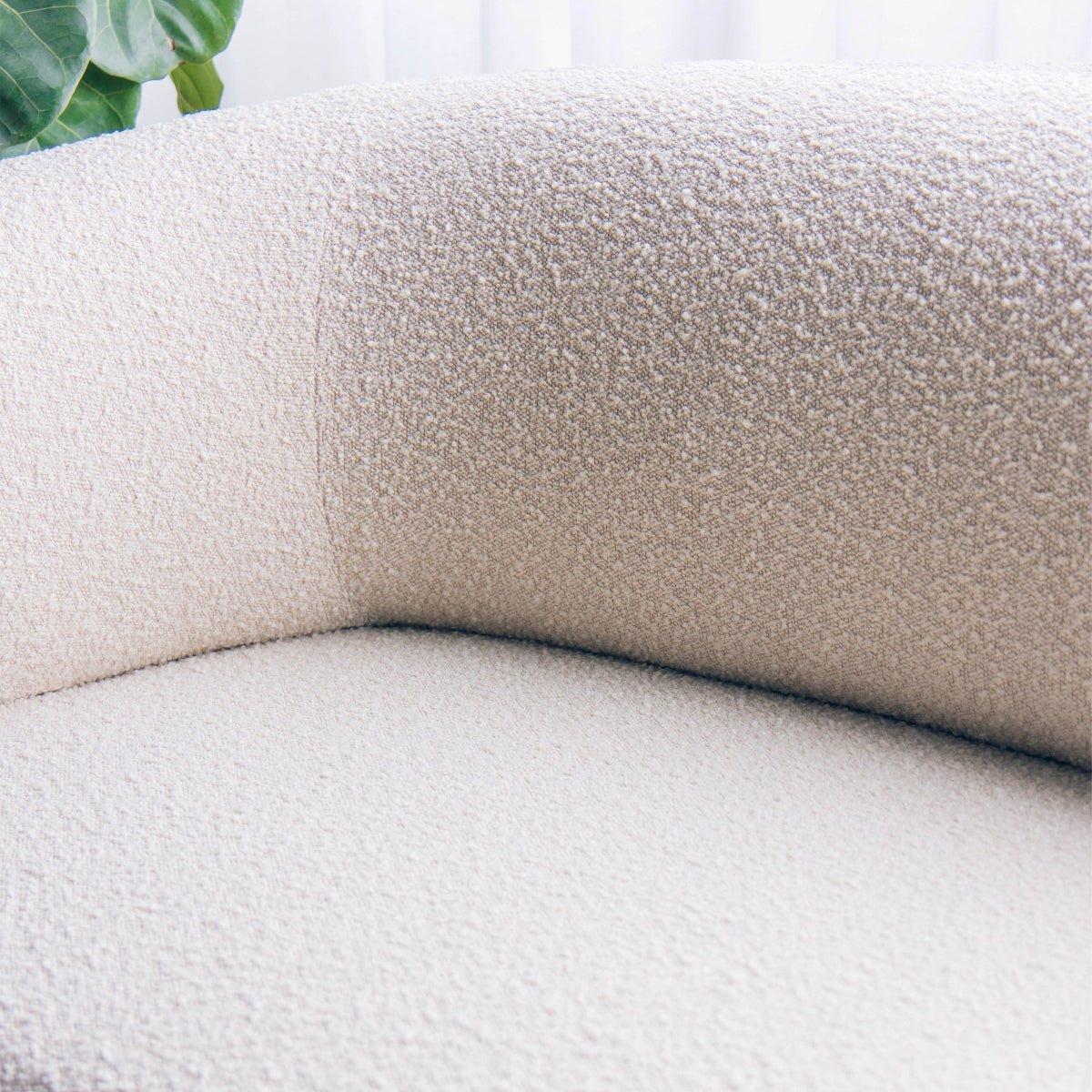Close-up of a textured beige sofa with a blurred green leaf in the corner.