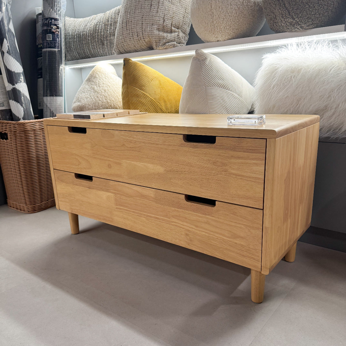 Wooden shoe cabinet with two drawers in a room setting with pillows and a basket.