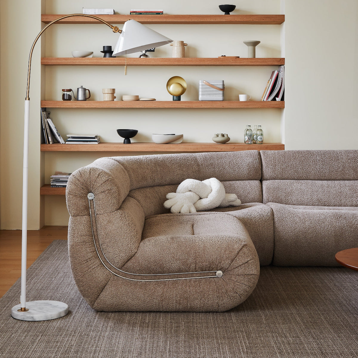 Modern living room with a beige sectional sofa, wooden shelves, and decorative items.