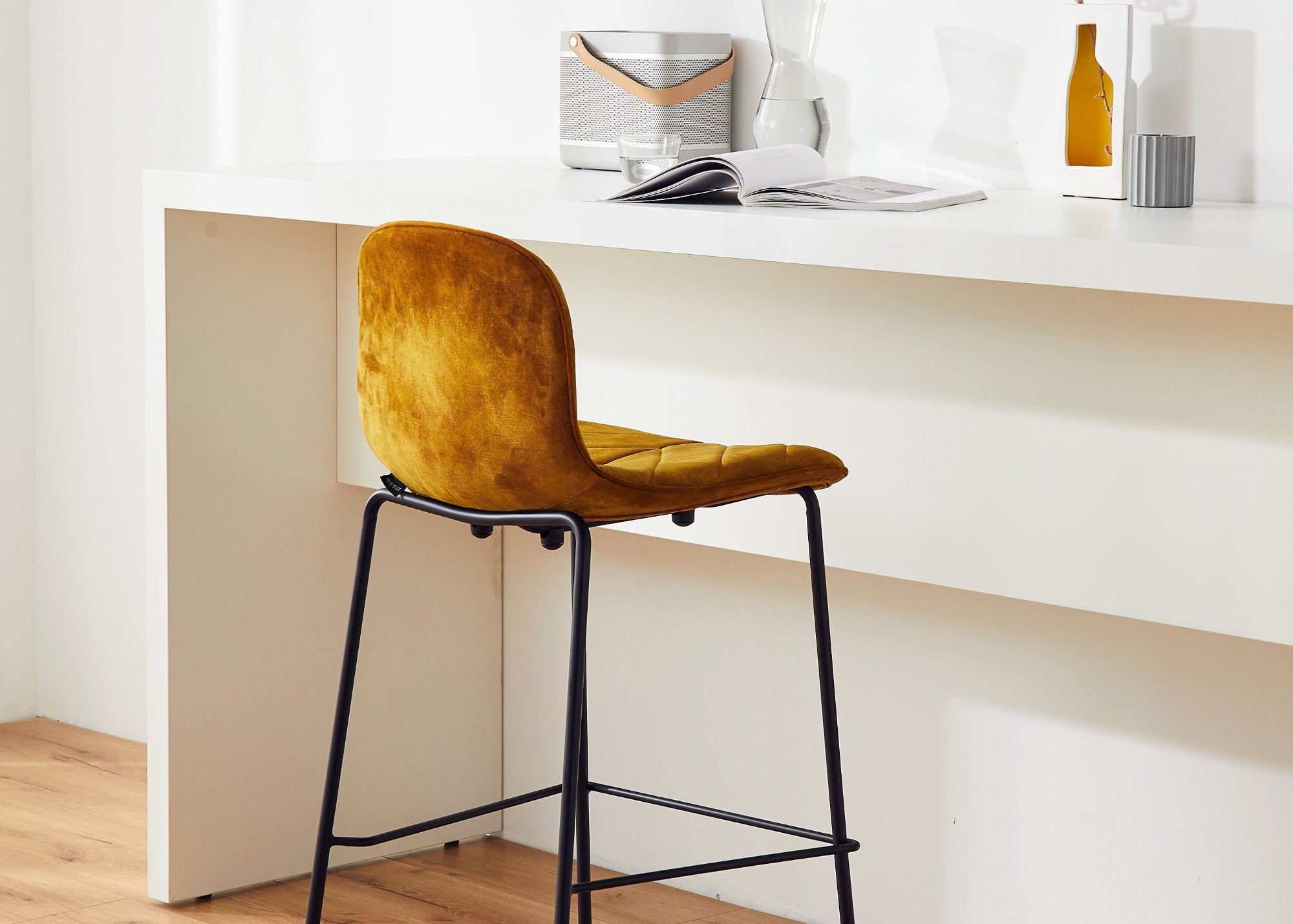 Yellow bar stool in front of a white desk with a clock on the wall.