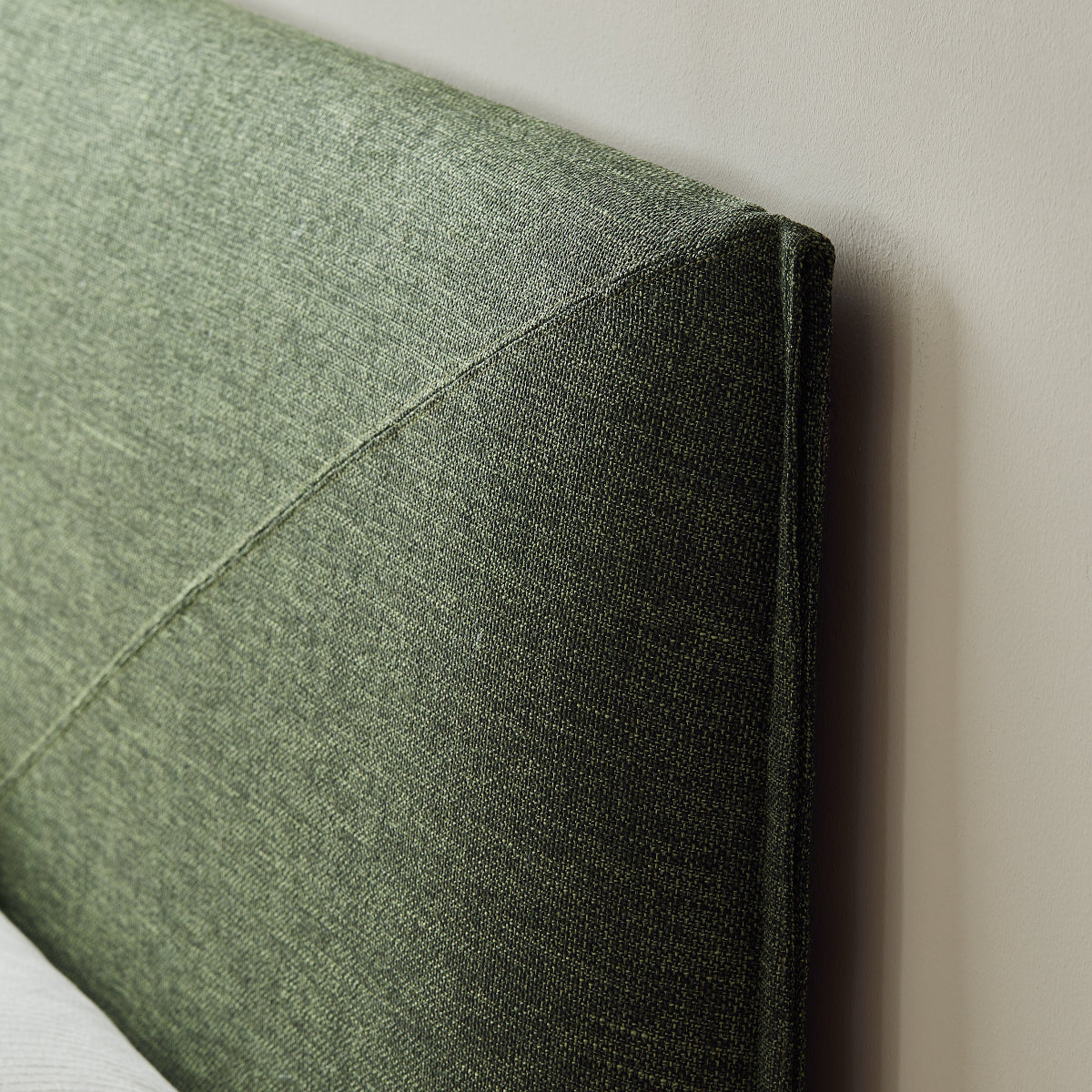 Green upholstered headboard against a plain wall