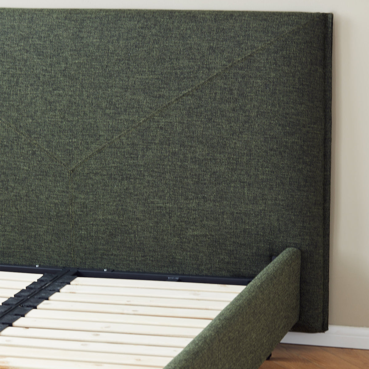 Green upholstered bed frame with wooden slats on a wooden floor.
