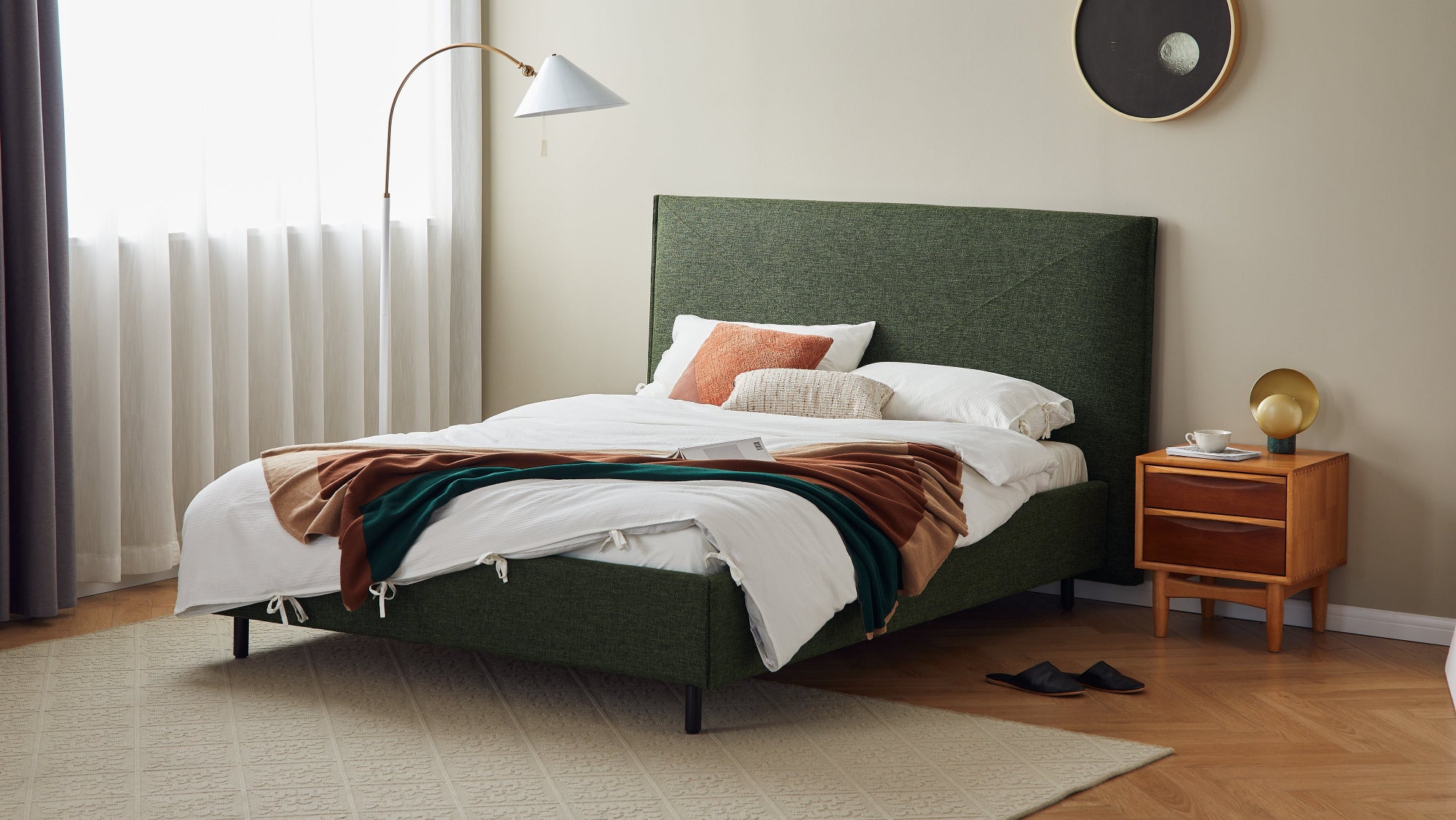 Modern bedroom with a green upholstered bed, wooden nightstand, and decorative items.