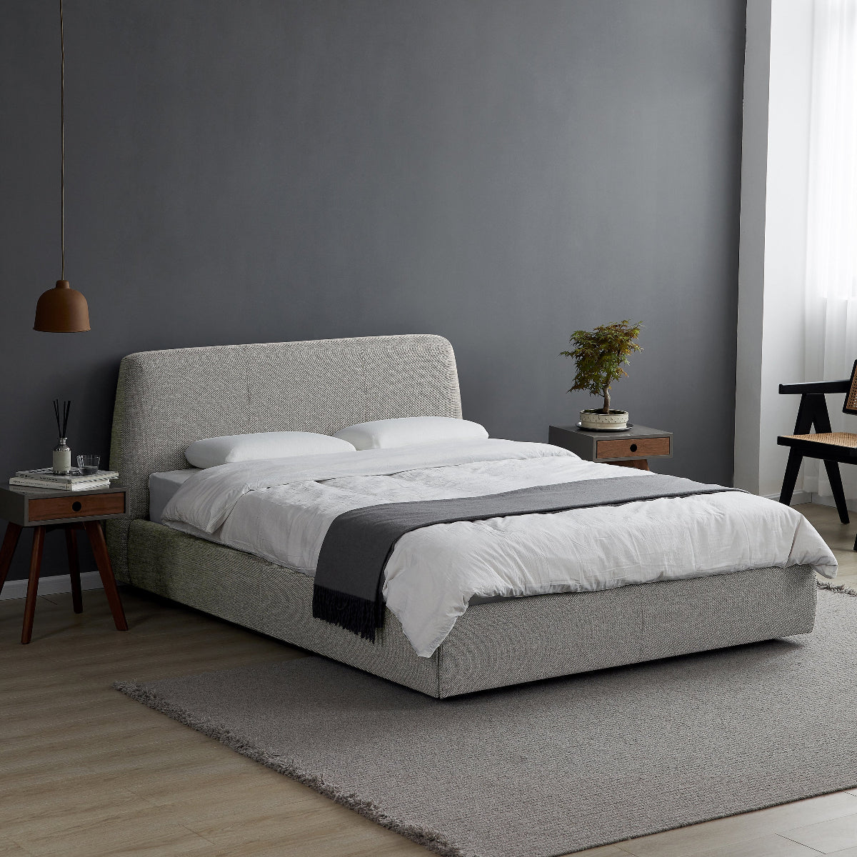 Gray upholstered bed in a modern bedroom with gray walls and wooden flooring.