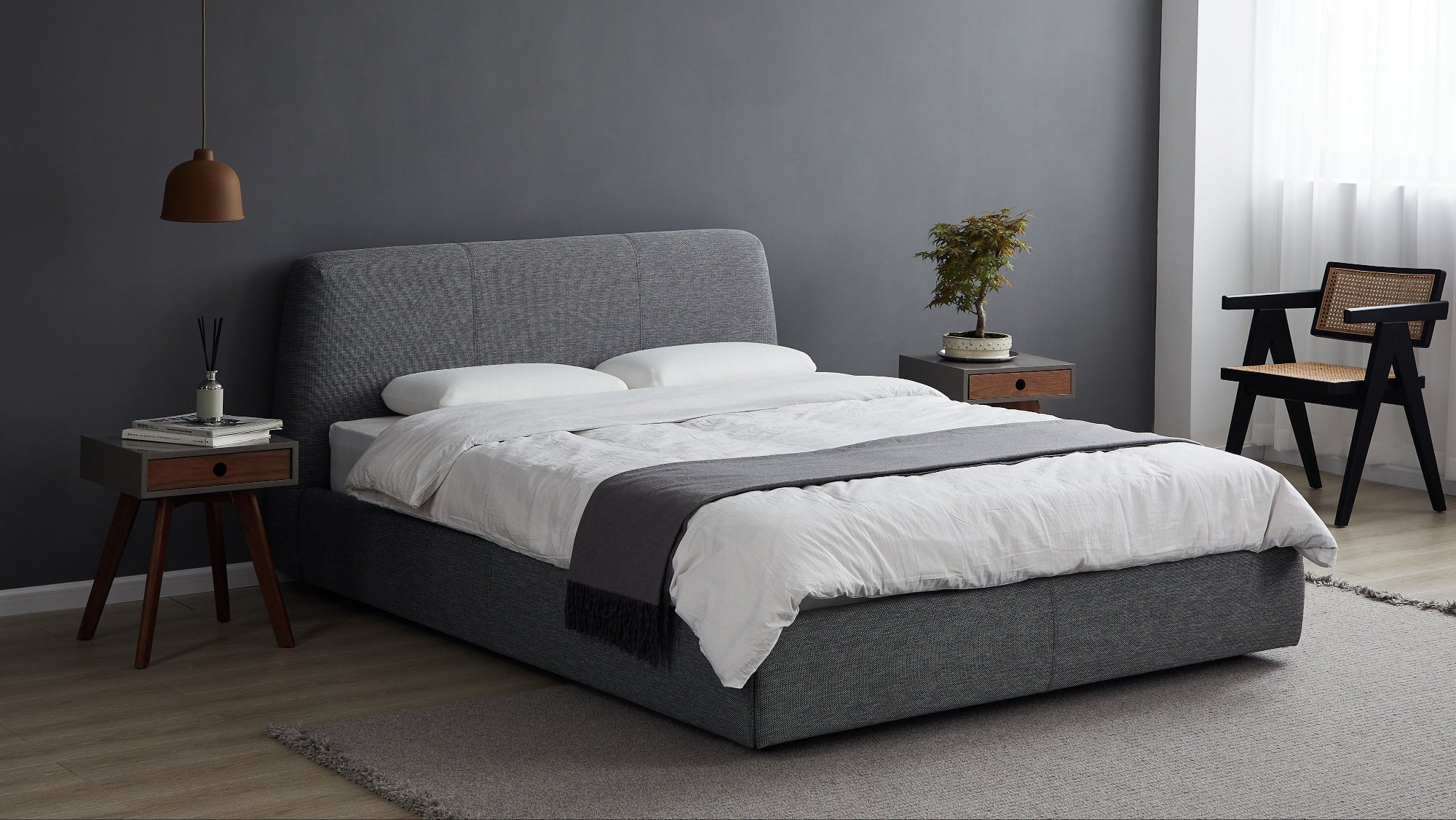 Gray upholstered bed with white bedding in a room with a dark gray wall and wooden floor.