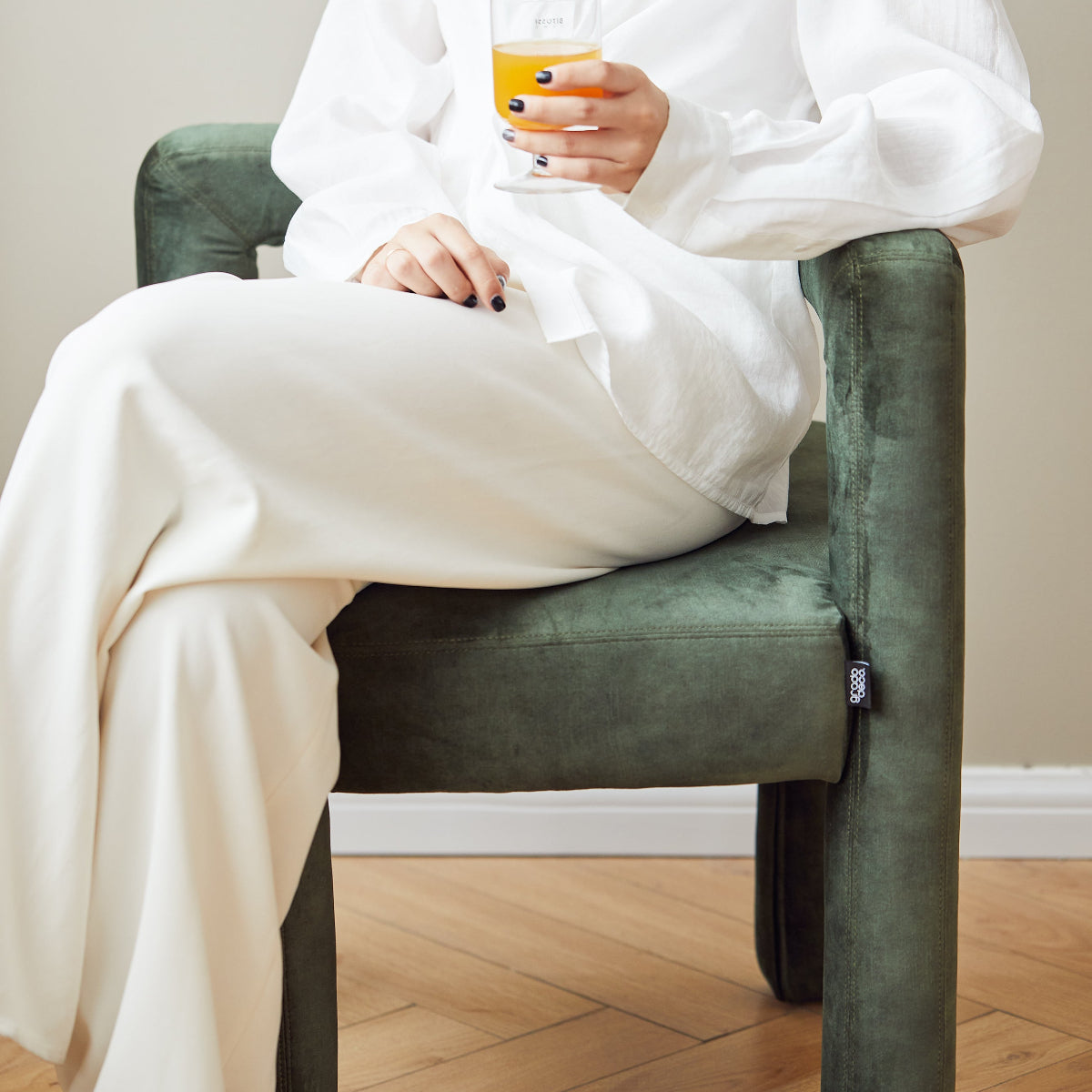 Person in a white robe sitting on a green chair holding a cup.