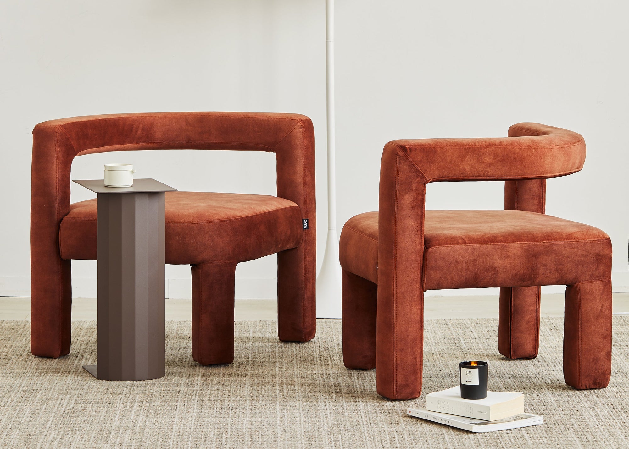 Two brown chairs and a small table in a minimalistic room with a white lamp.