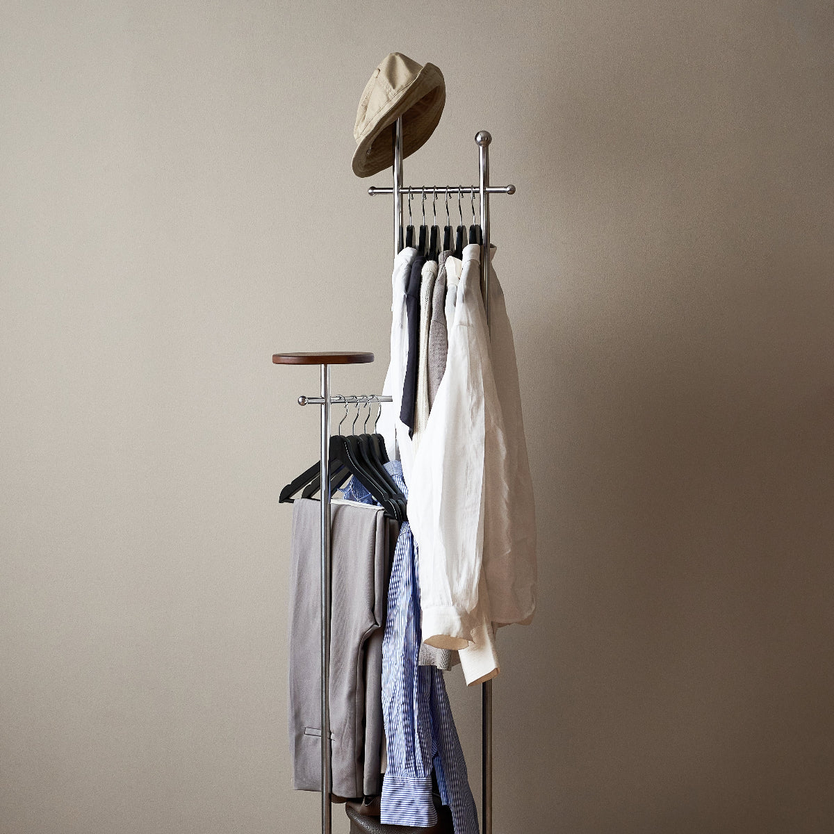 Clothing rack with hats and shirts against a beige wall