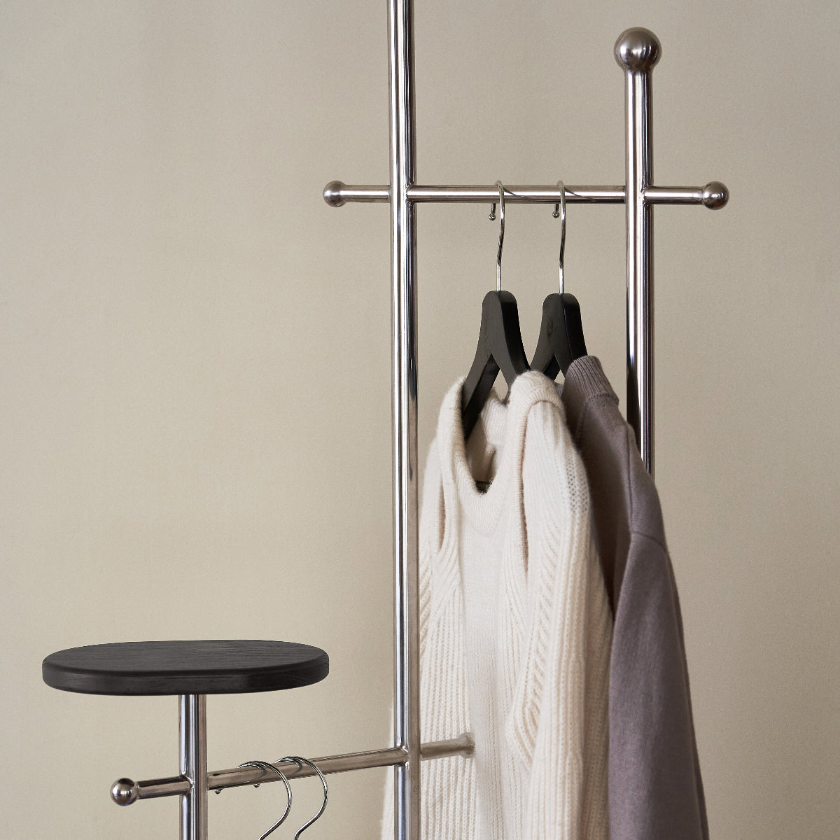Metal clothing rack with hangers holding shirts against a beige wall.